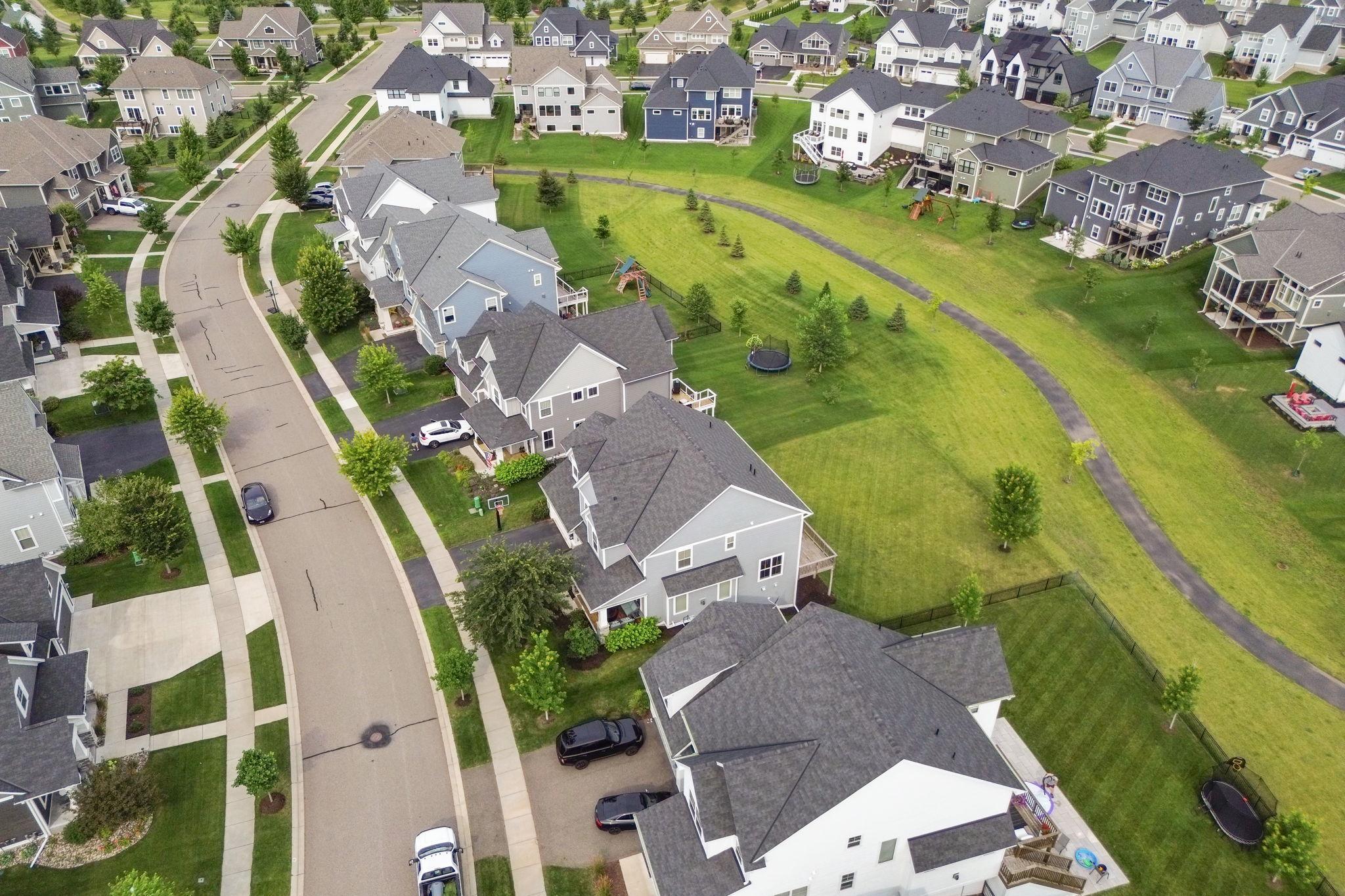 Aerial view of homes bordering a broad grassy greenway and paved walking path.