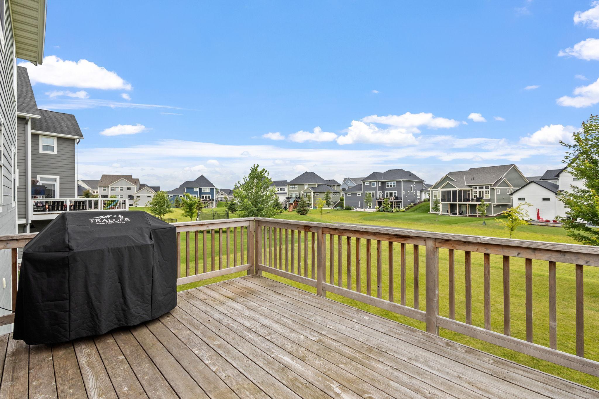 Wooden deck with a covered grill overlooks a green lawn and neighboring homes.