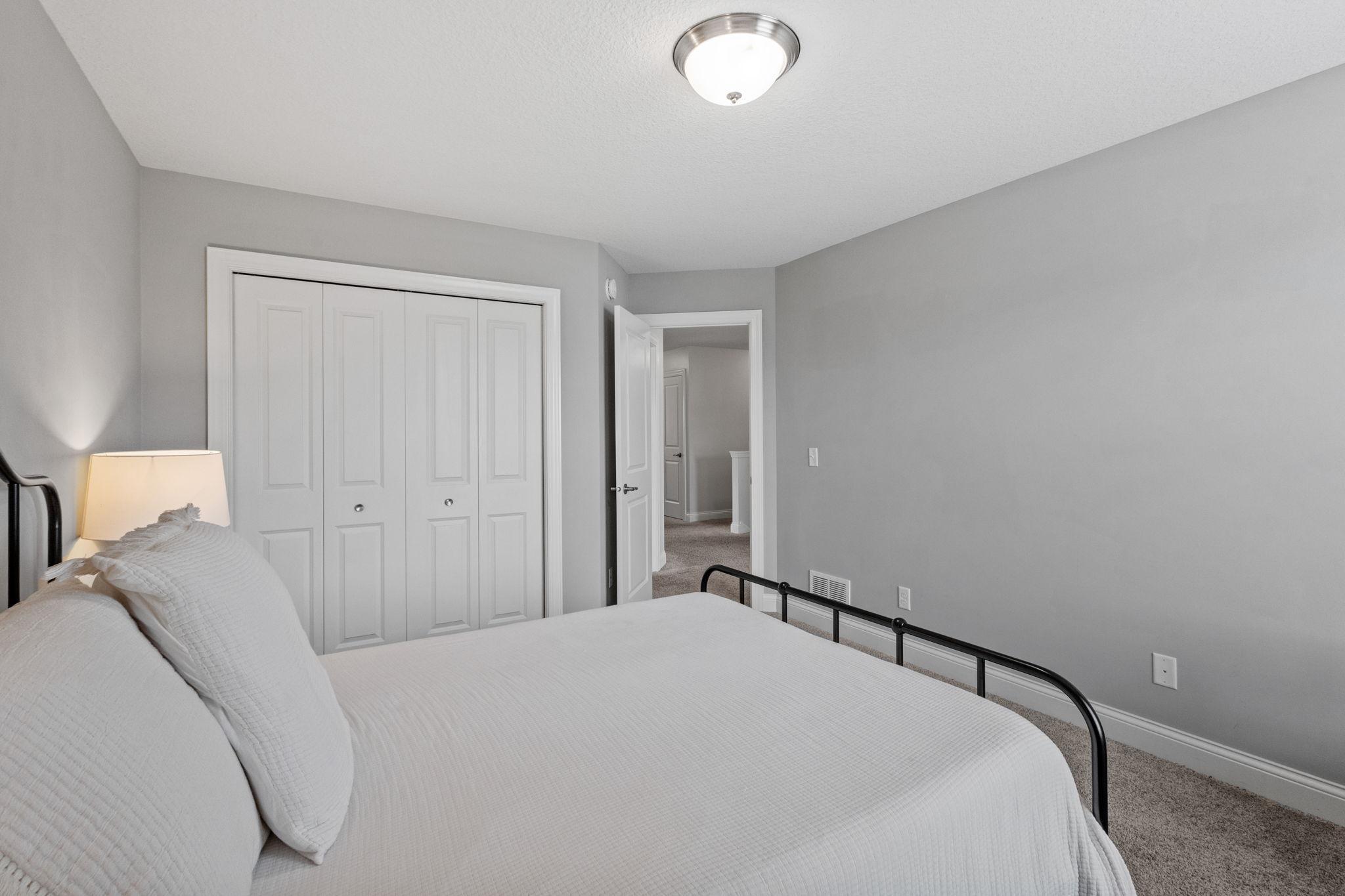 Bedroom with a white bed, black metal frame, gray walls, and a wide closet with folding doors.