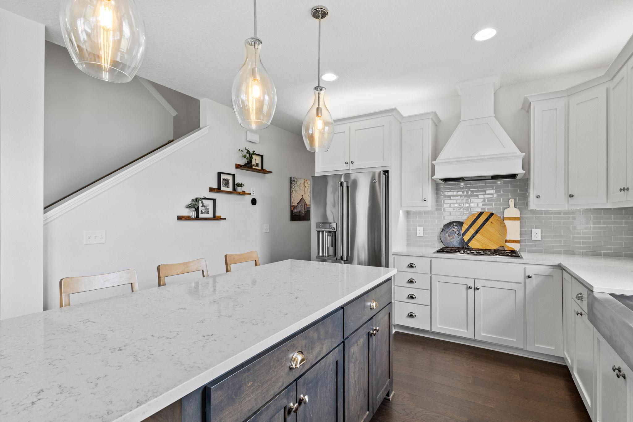 Kitchen with a large dark blue island, white stone countertop, and glass pendant lights.
