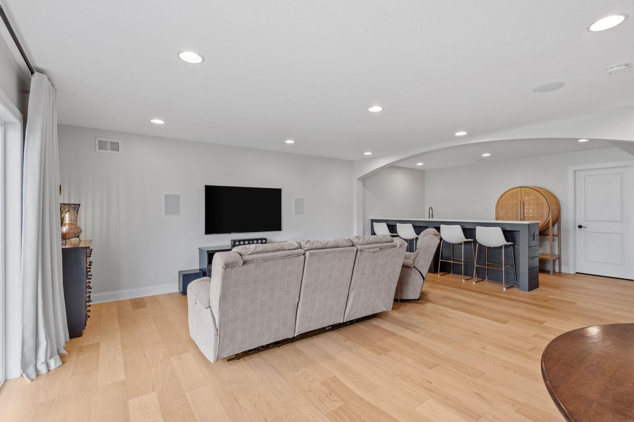 Living room with a large sectional facing a wall-mounted TV beside a bar island with four stools.
