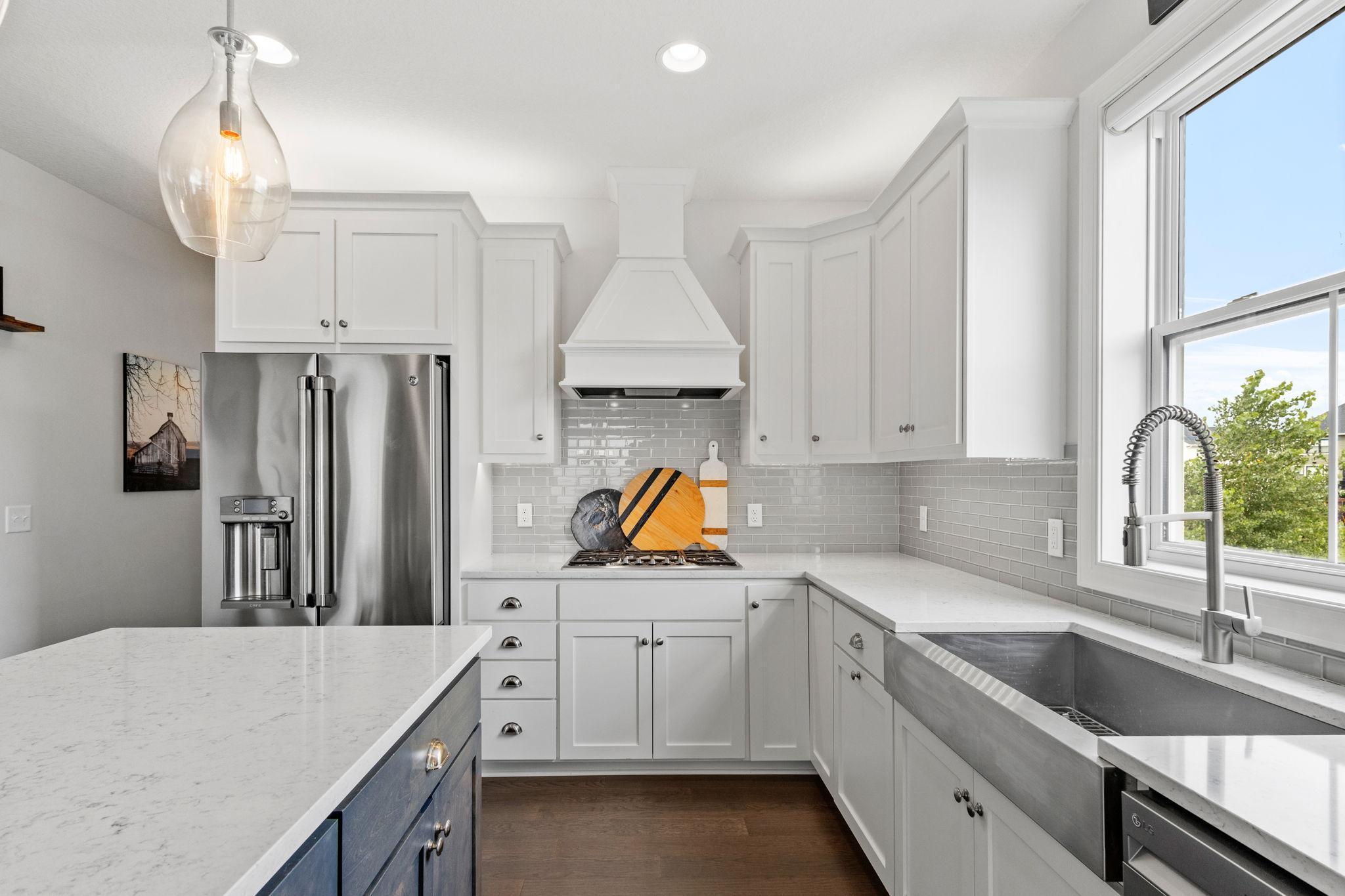 Bright kitchen with white cabinets, gray tile backsplash, quartz counters, and a large farmhouse sink.