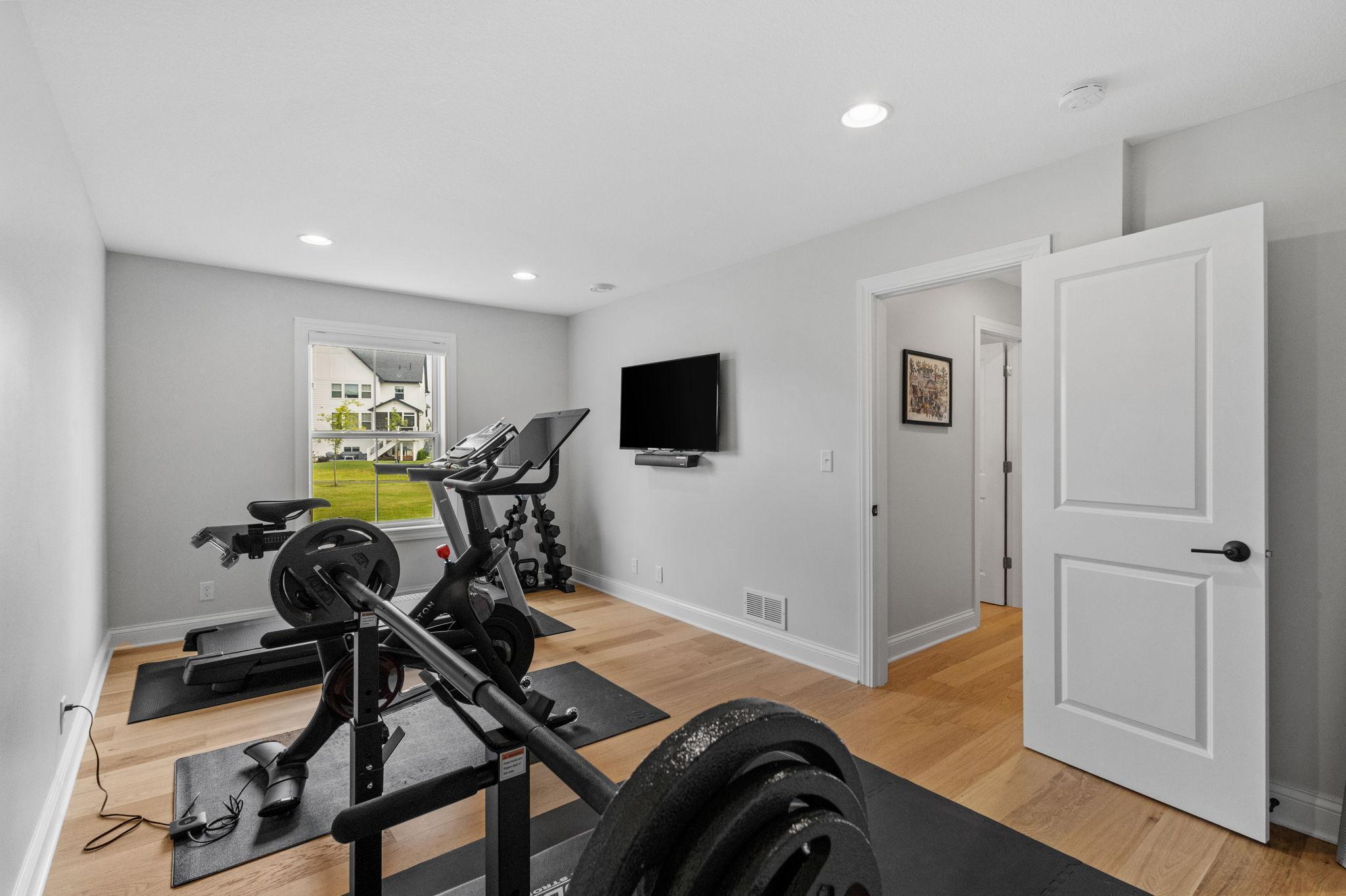 Home gym with weightlifting equipment, exercise bikes, and a wall-mounted television.