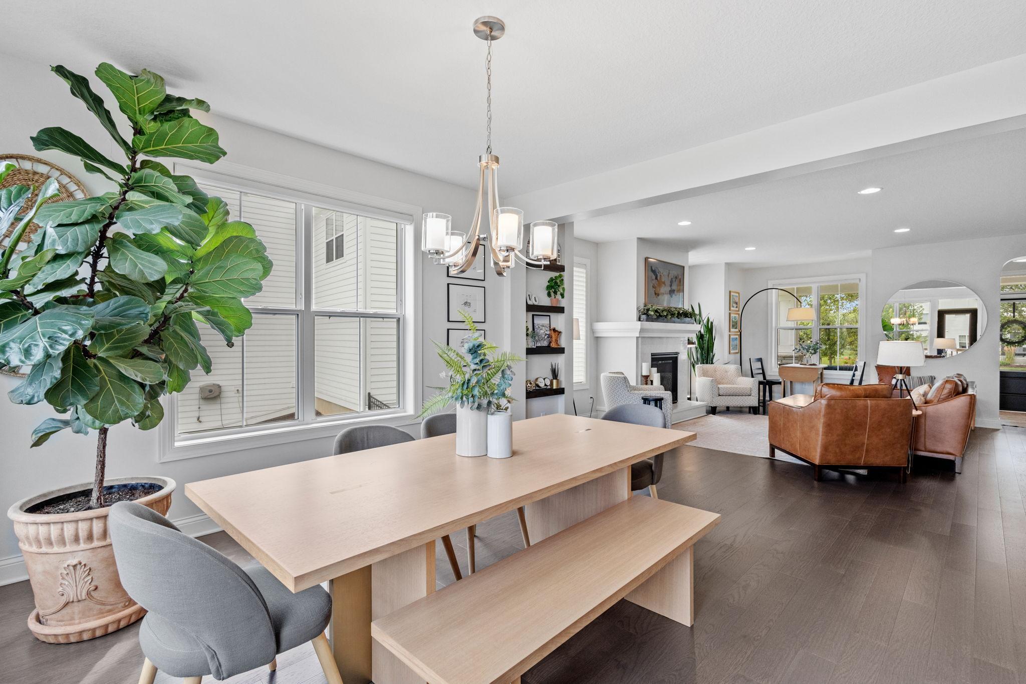 Open dining and living area with a wood table, chandelier, fireplace, and brown leather seating.