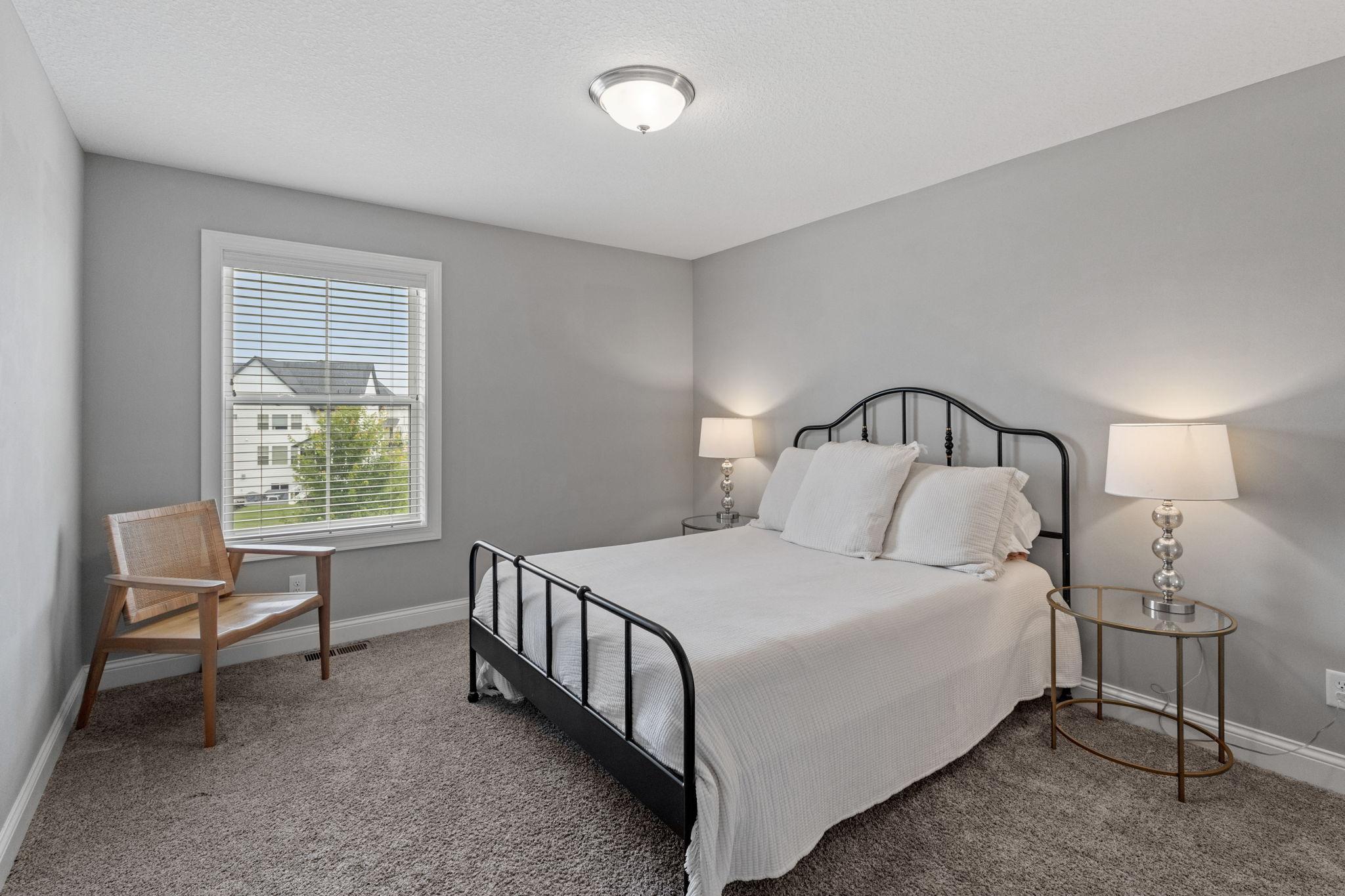 Bedroom with a black metal bed frame, white bedding, and a wooden chair beside the window.