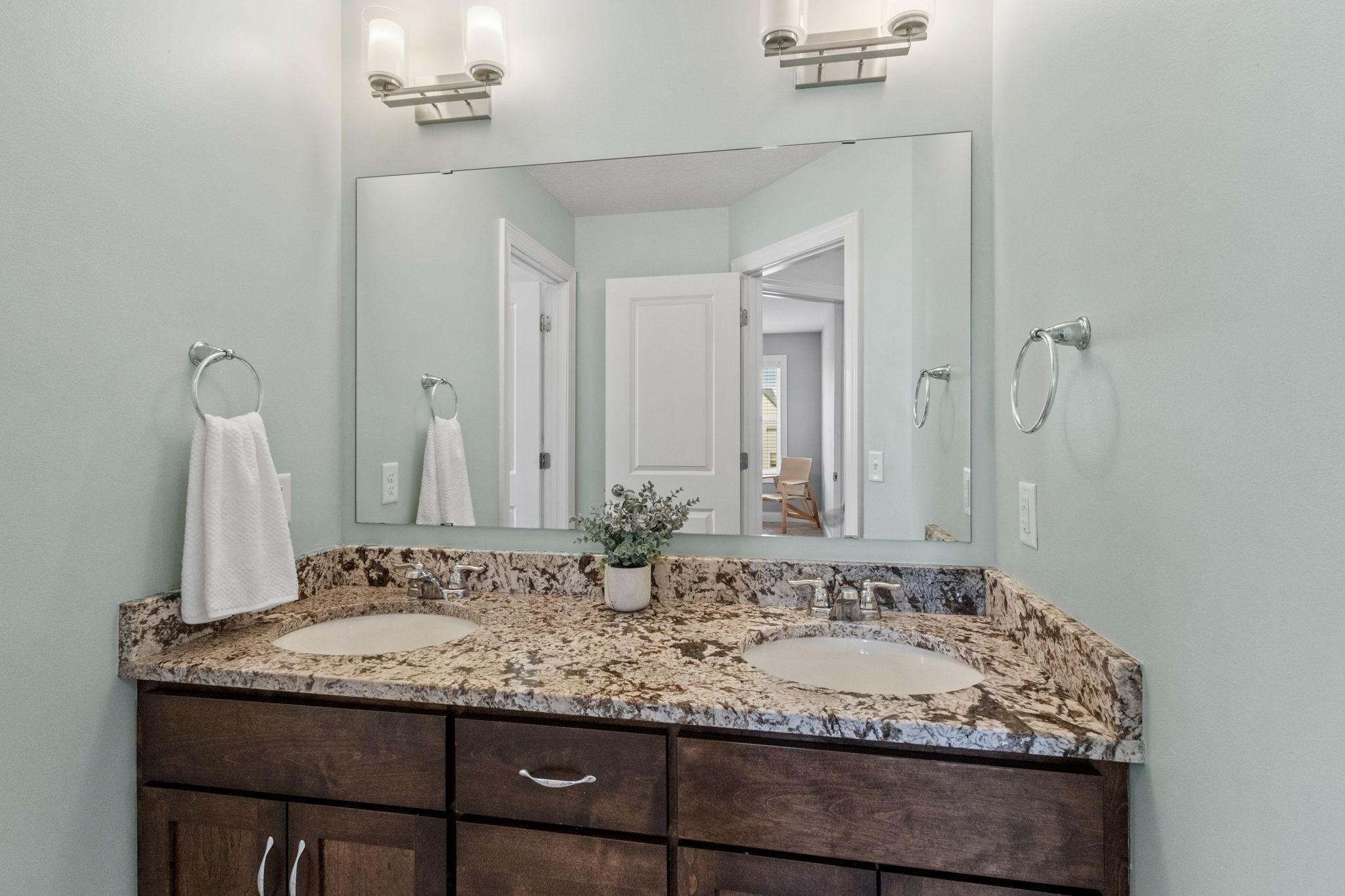 Bathroom with a double-sink granite vanity, dark wood cabinets, and a wide mirror.