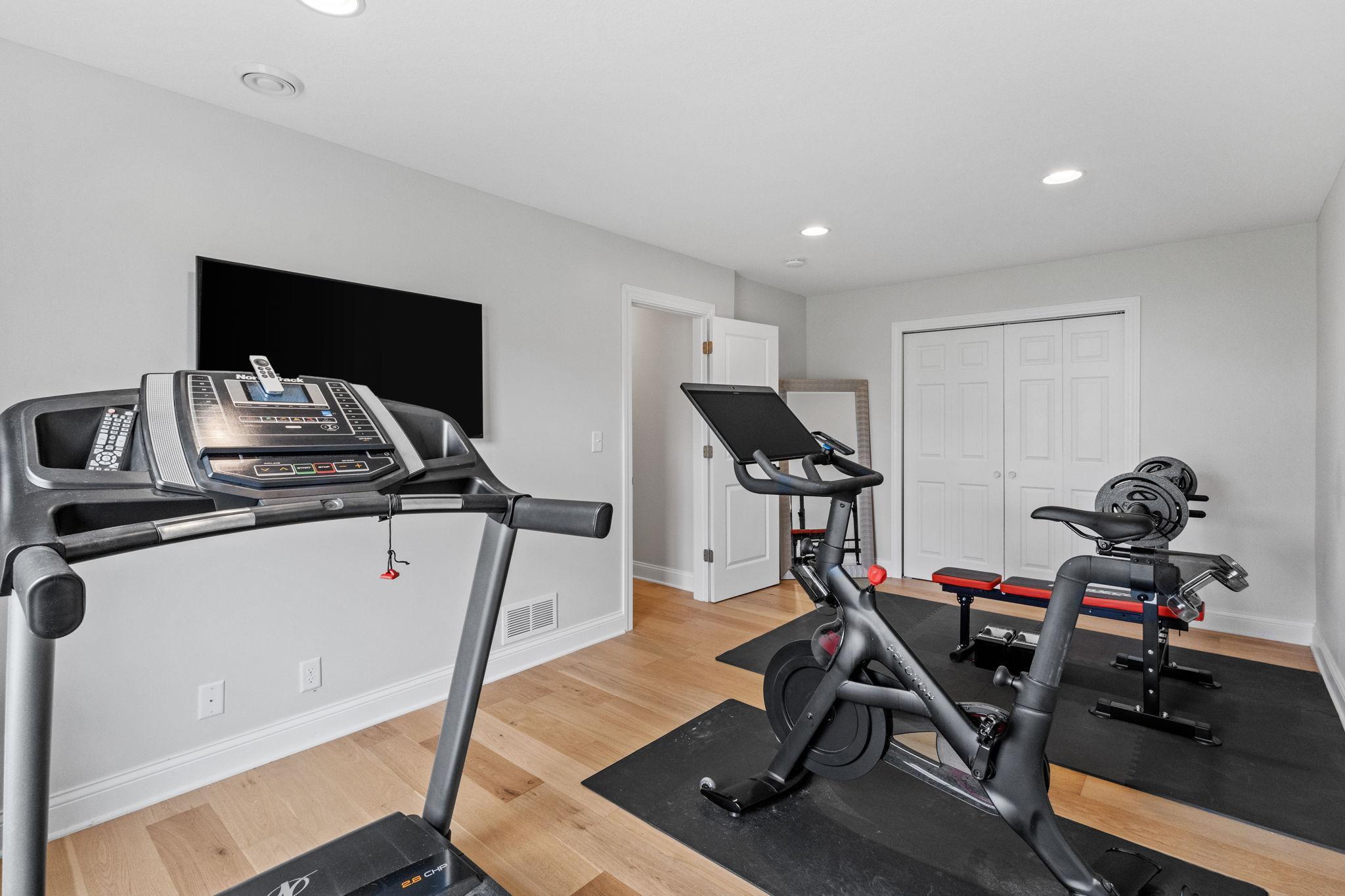 Home gym with a treadmill, exercise bike, and weight bench on black mats.