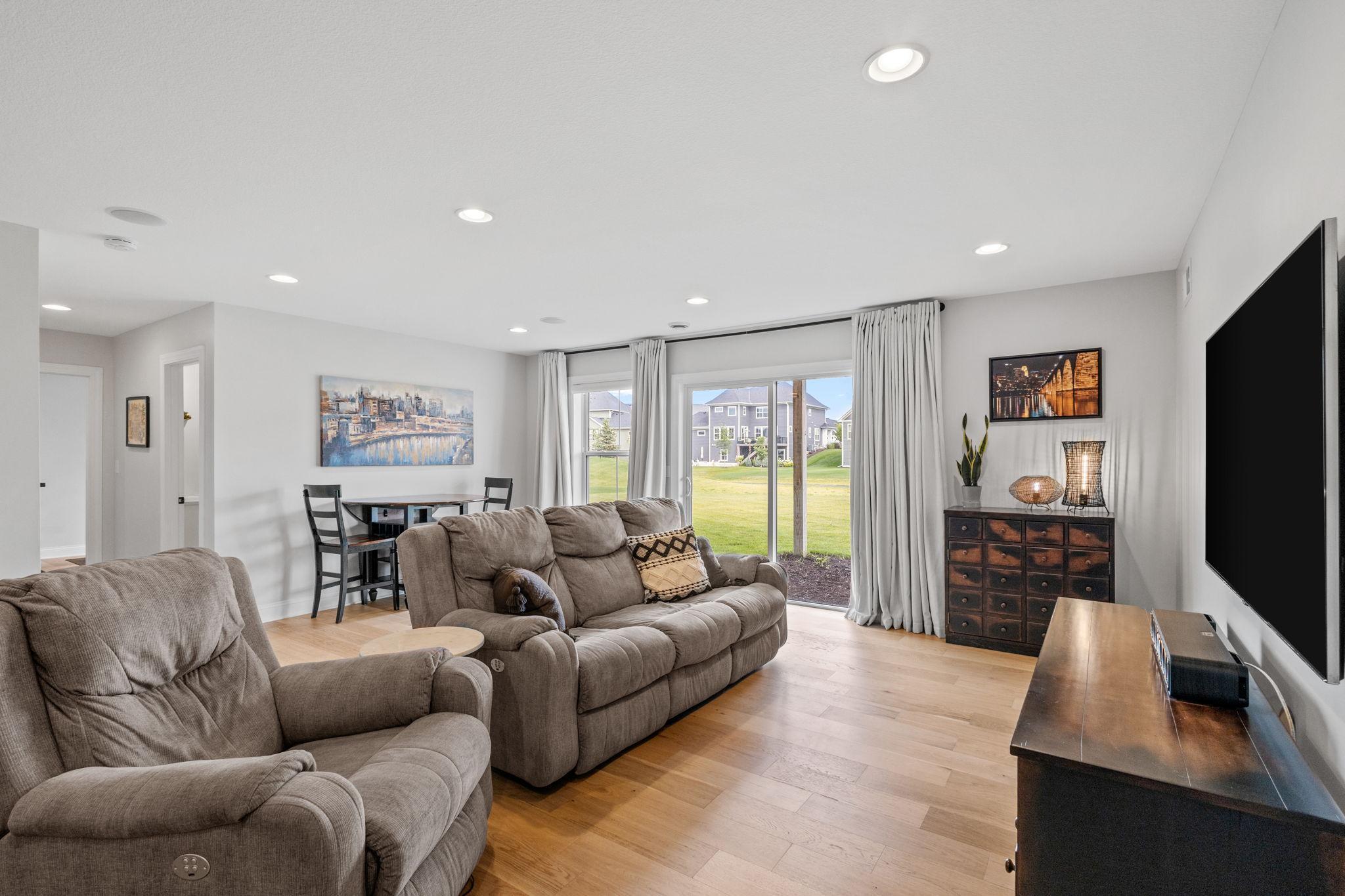 Living room with taupe reclining sofas, wood floors, and sliding doors opening to a lawn.