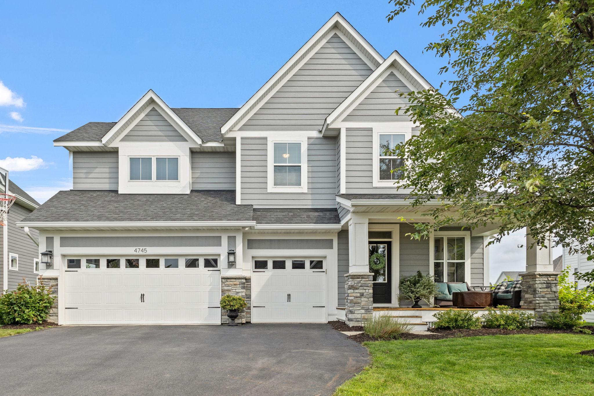 Gray two-story home with white trim, two garage doors, and a covered porch with outdoor seating.