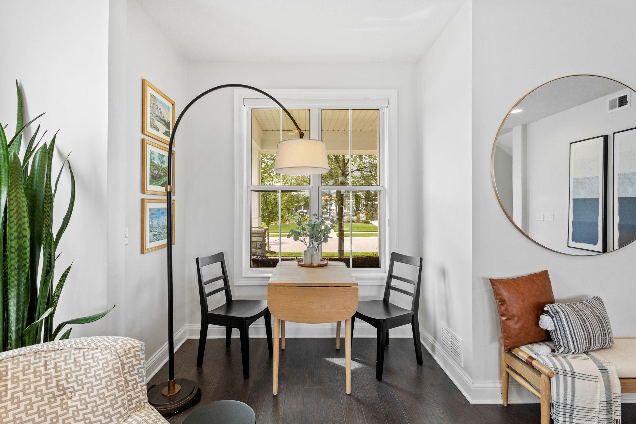 Dining nook with a small wood table and two black chairs beside a large window.