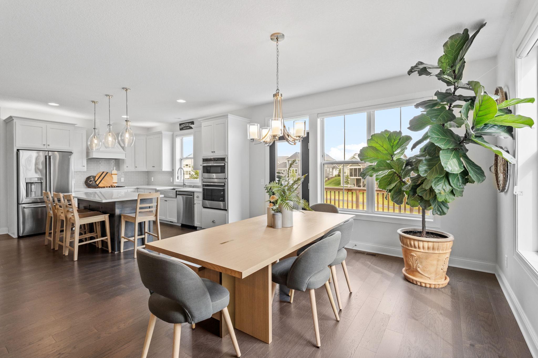 Open kitchen and dining area with white cabinets, a large wood table, and windows facing the backyard.