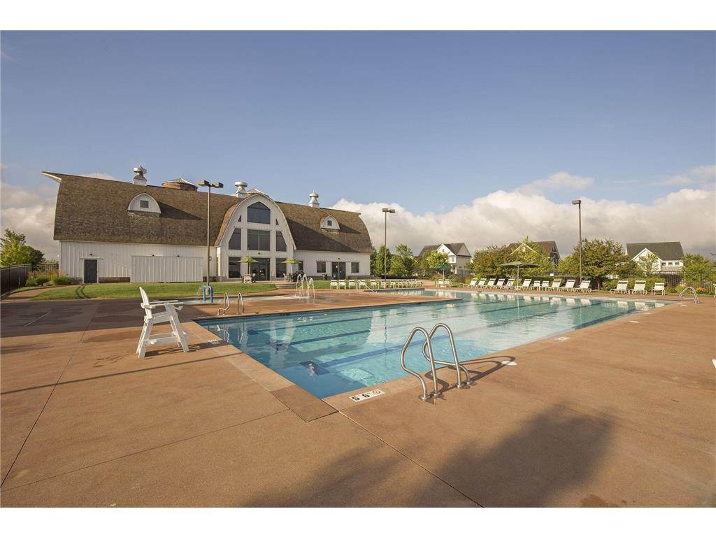 Outdoor community pool beside a clubhouse, with lounge chairs and a sunny deck.