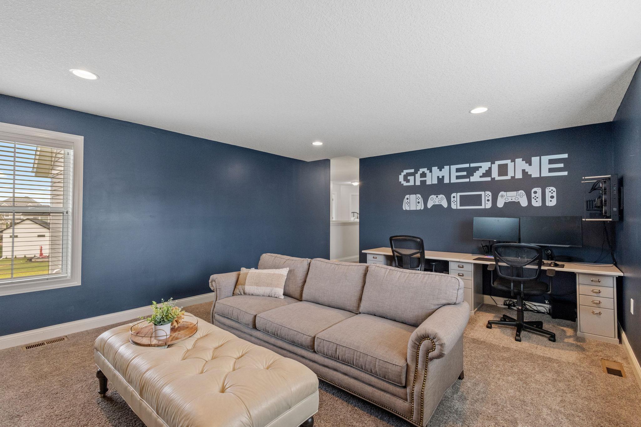 Furnished game room with a gray sofa, computer desk, and GAMEZONE wall decal.
