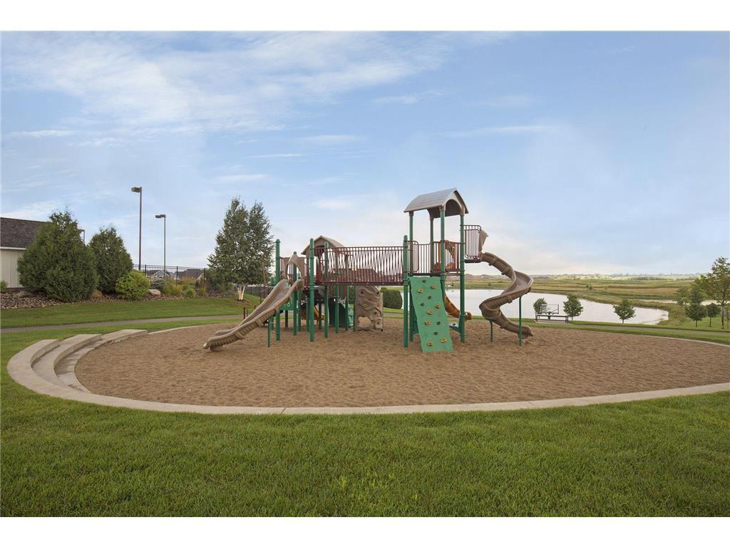 Outdoor playground with climbing structure and slides beside a small pond and open fields.