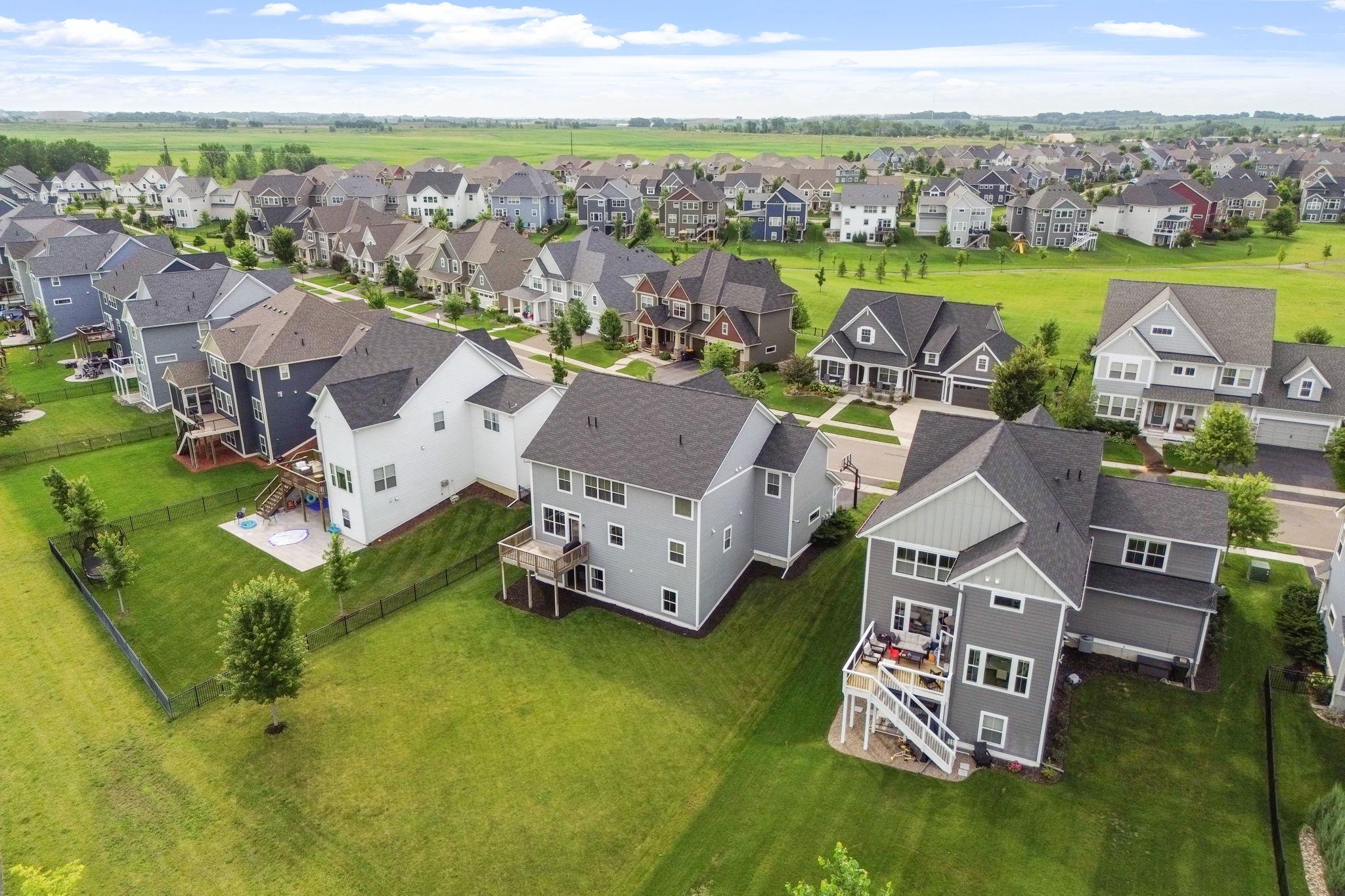 Aerial view of a gray two-story home with a deck and fenced lawn among neighborhood houses.