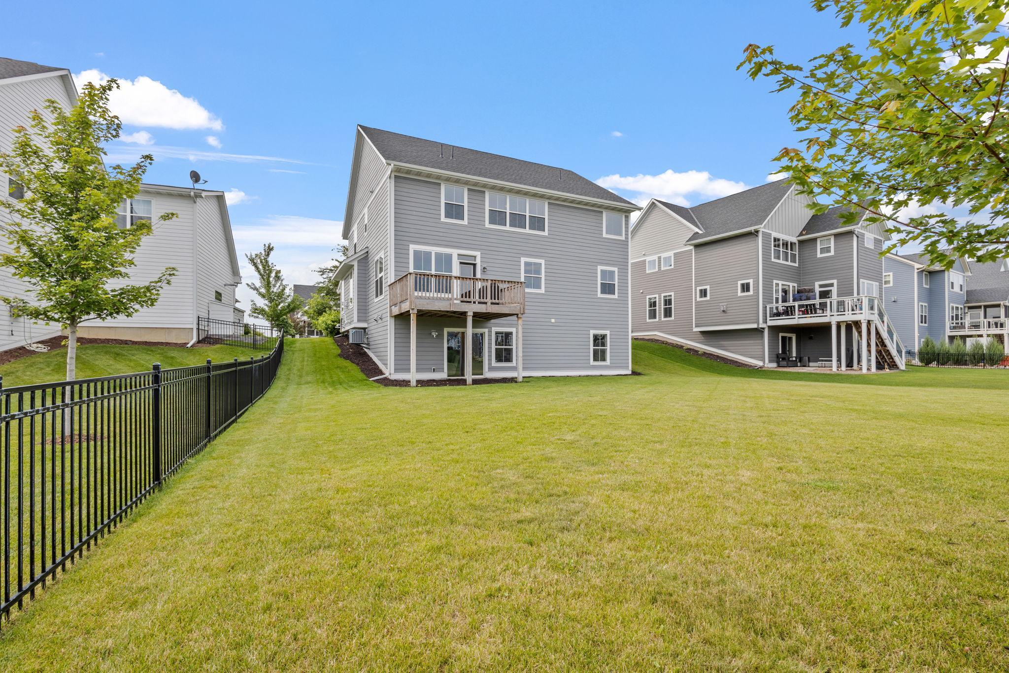 Rear of a gray two-story home with a raised wooden deck and broad grassy backyard.
