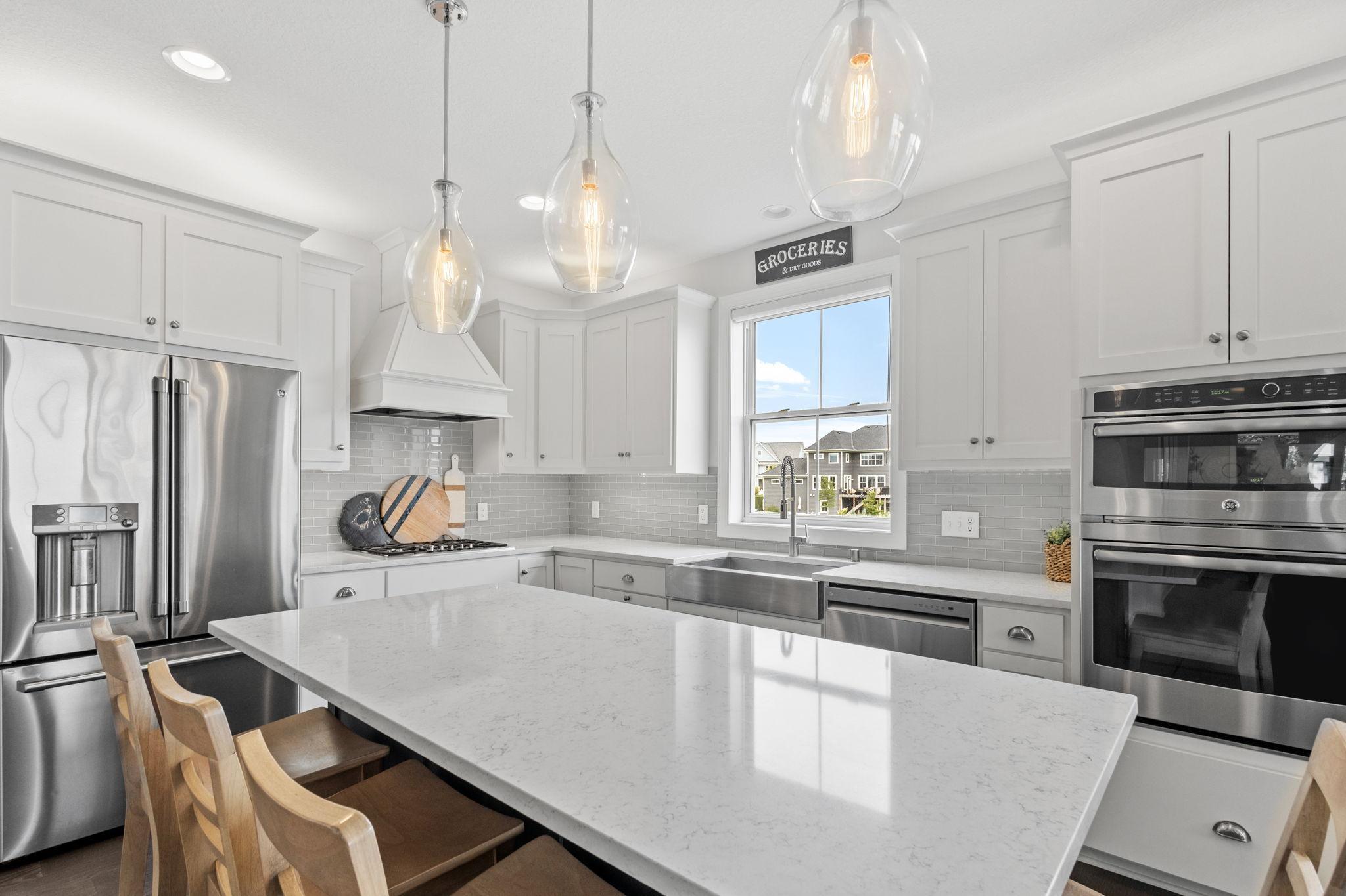 Bright white kitchen with a large island, stainless steel appliances, and pendant lights.