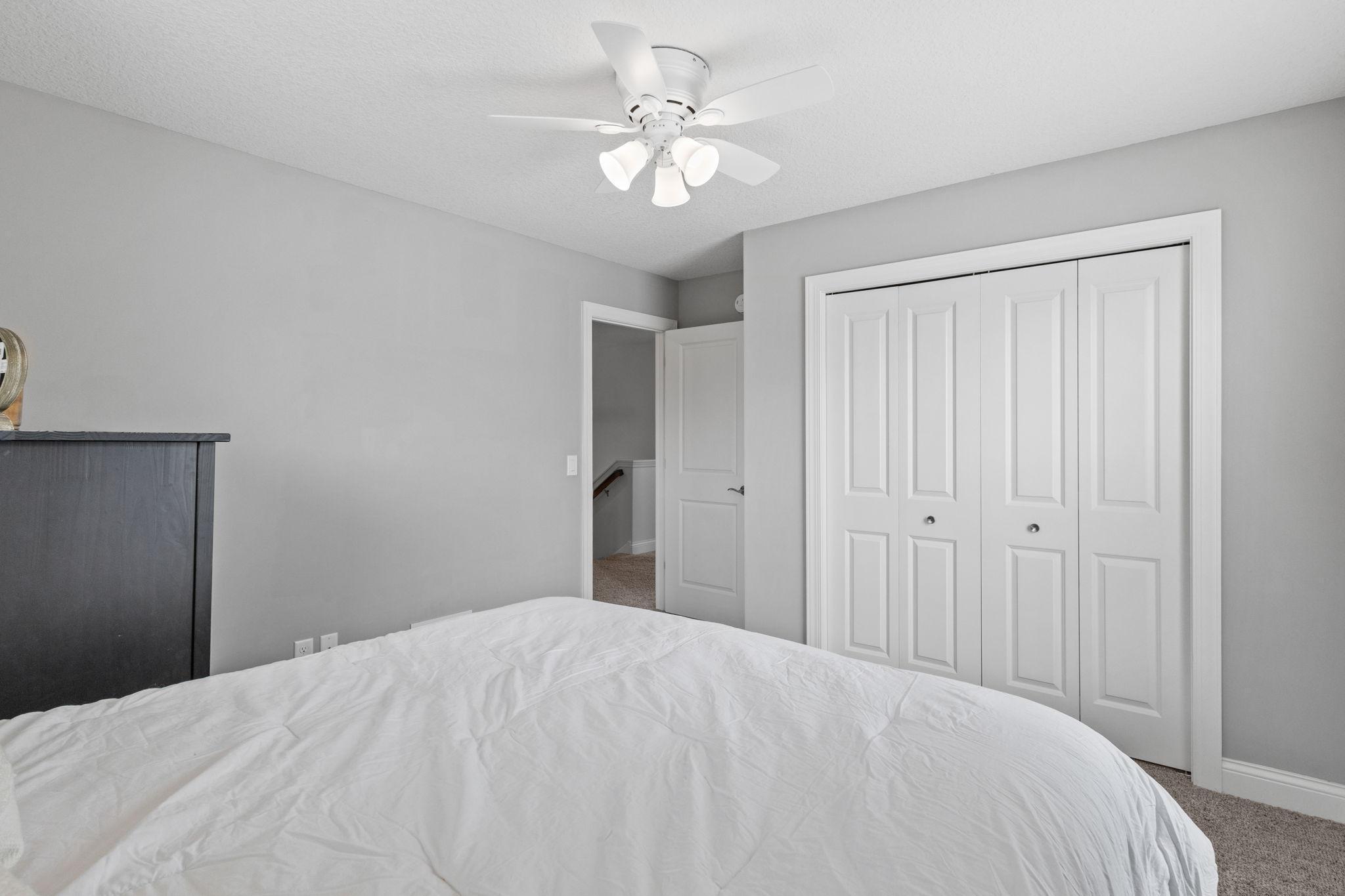 Bedroom with a white bed, gray walls, ceiling fan, and double closet doors.