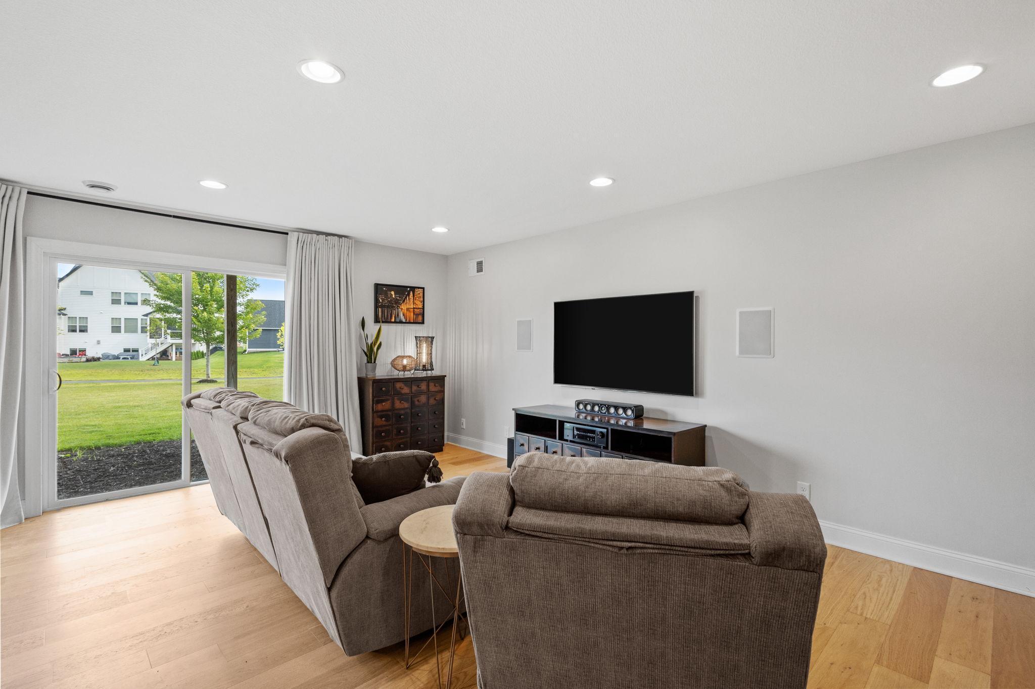 Living room with gray sectional seating, wall-mounted television, and sliding glass doors to the lawn.