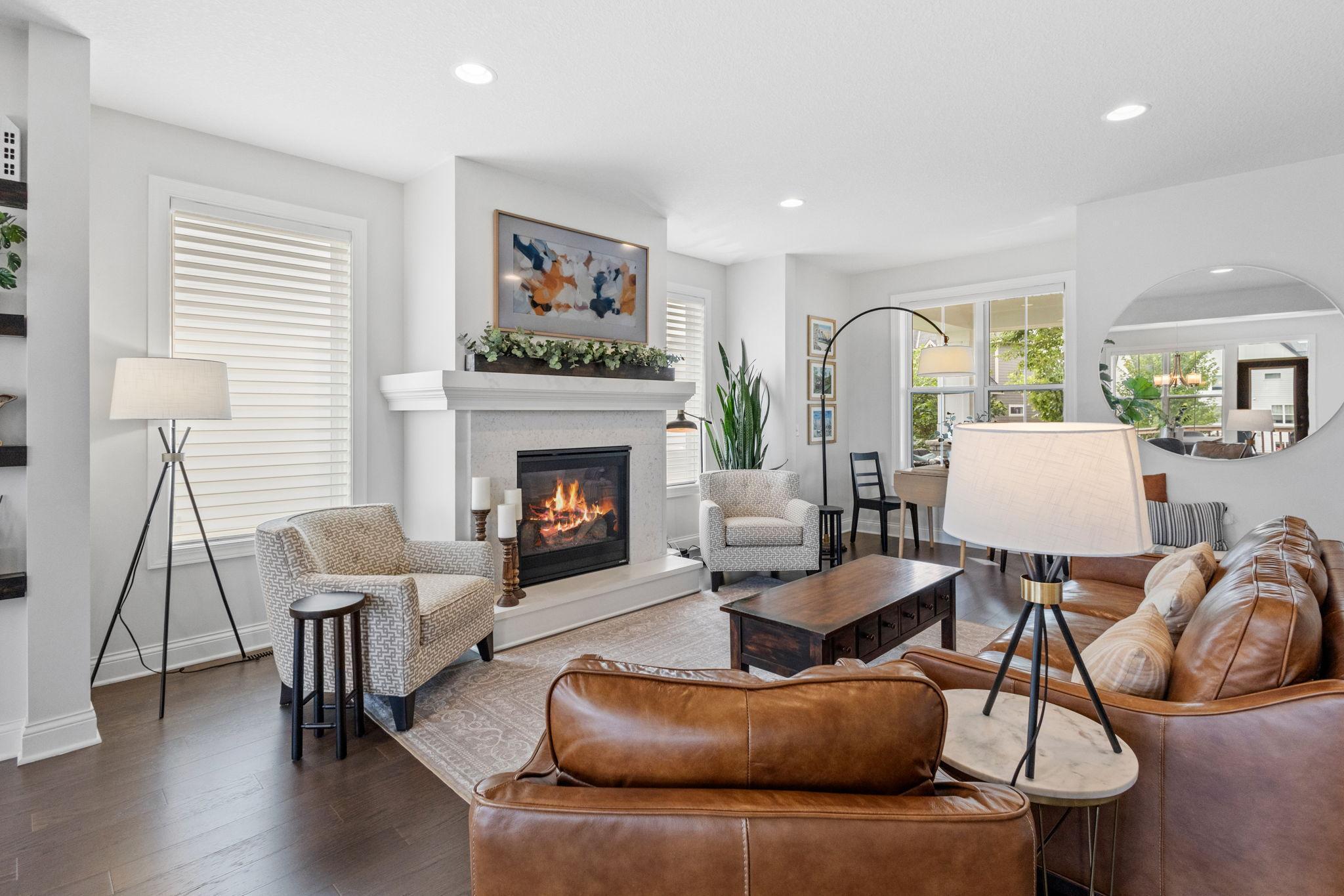 Living room with a lit fireplace, brown leather sofas, and a dining area by the windows.