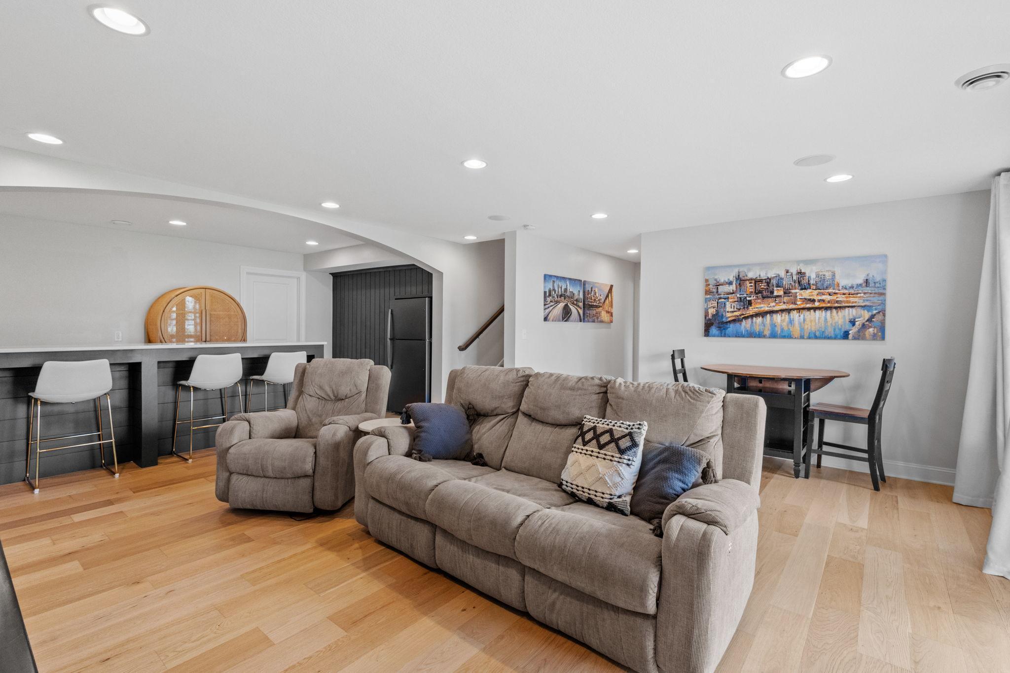 Open-plan living room with beige sectional, wood floors, kitchen island, and dining area.