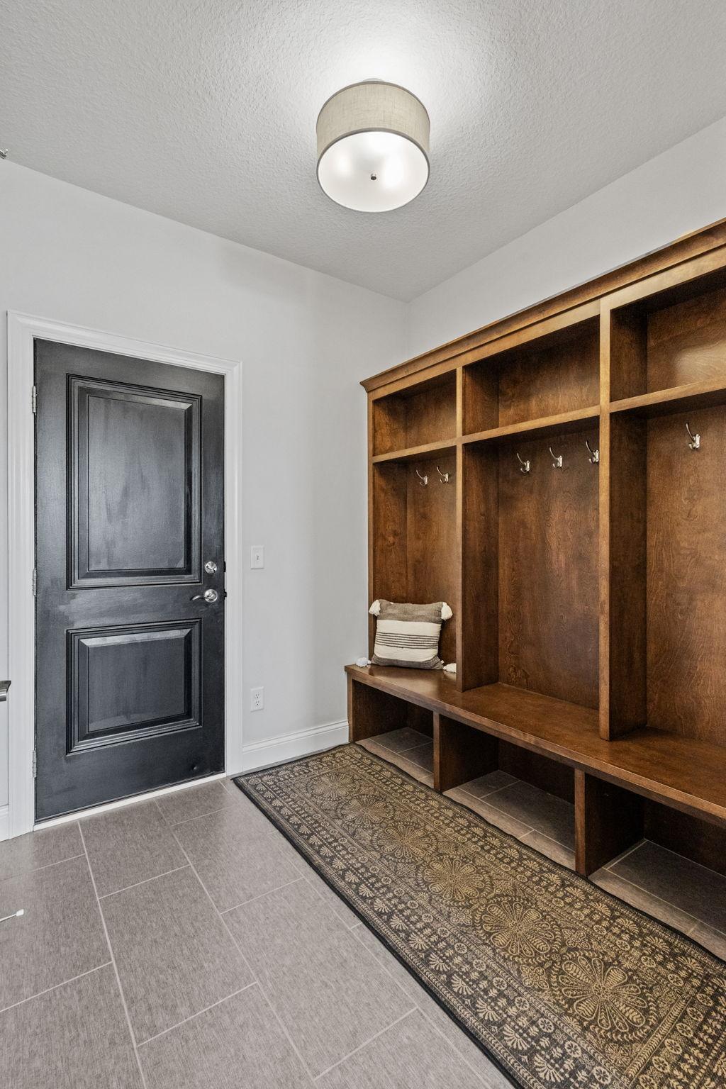 Entryway with built-in wood cubbies, hooks, and bench beside a dark paneled door.