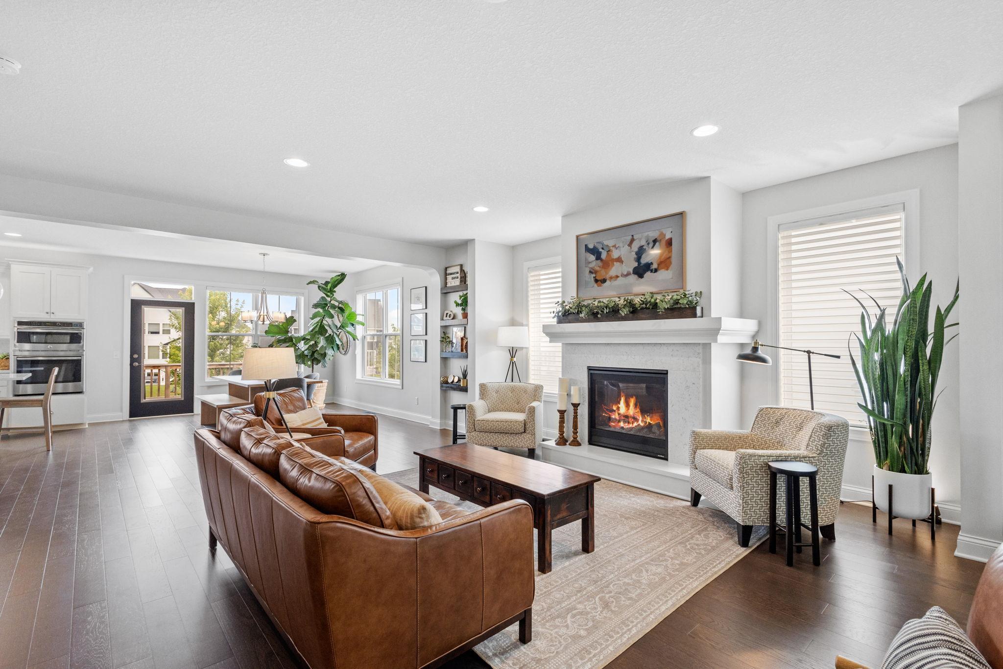 Open-plan living room with a lit fireplace, brown leather sofas, and large windows.