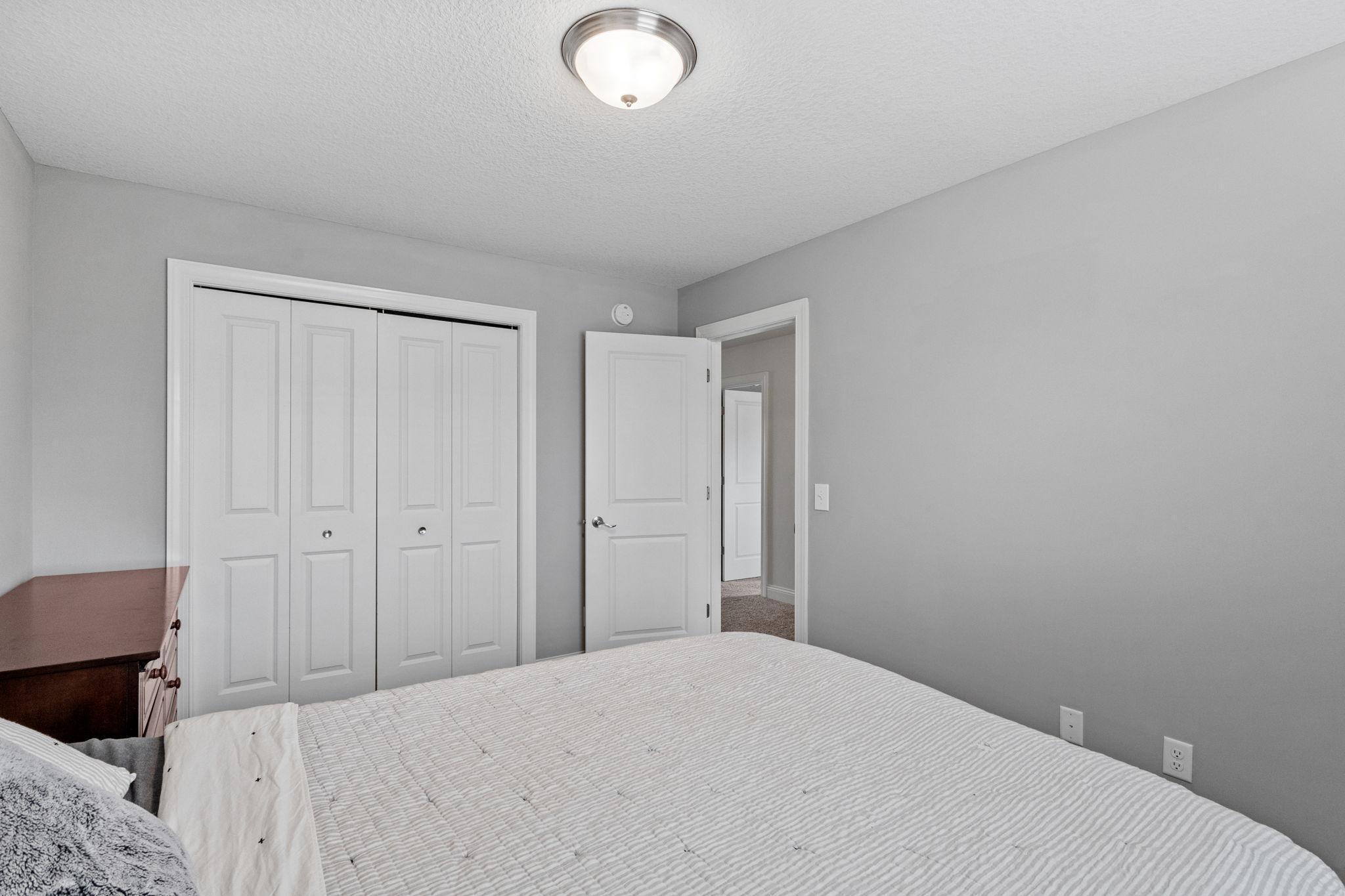 Bedroom with a white quilted bed, dark wood dresser, and white closet doors.