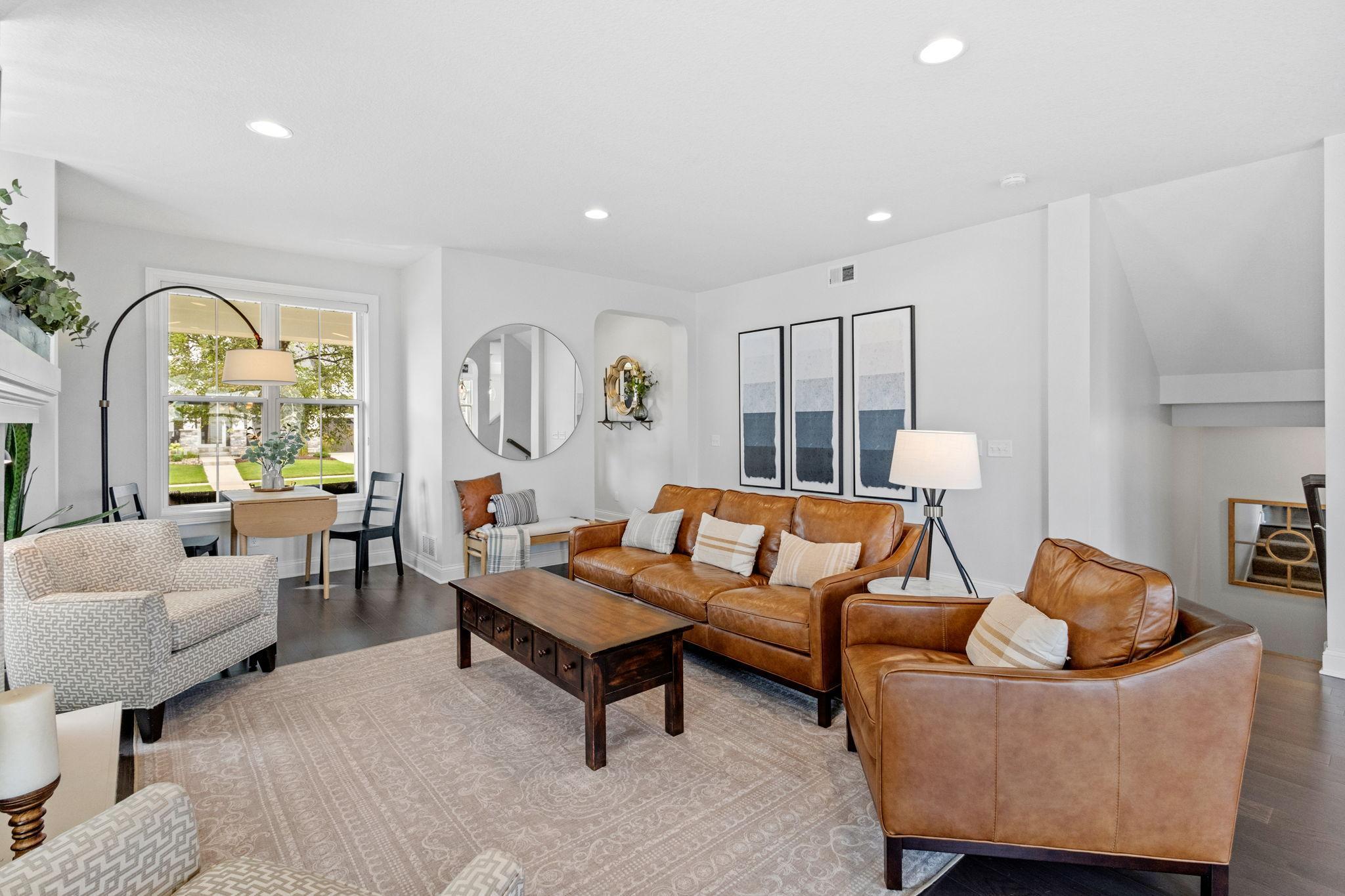 Staged living room with caramel leather seating, patterned chairs, and a large window