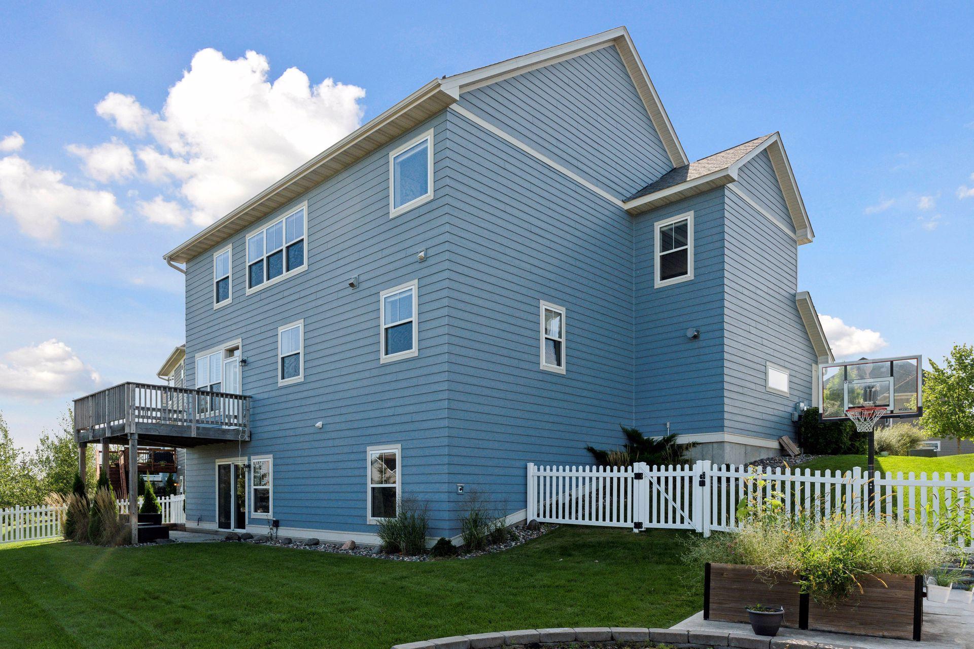 Blue two-story home with a raised deck, white picket fence, and basketball hoop.