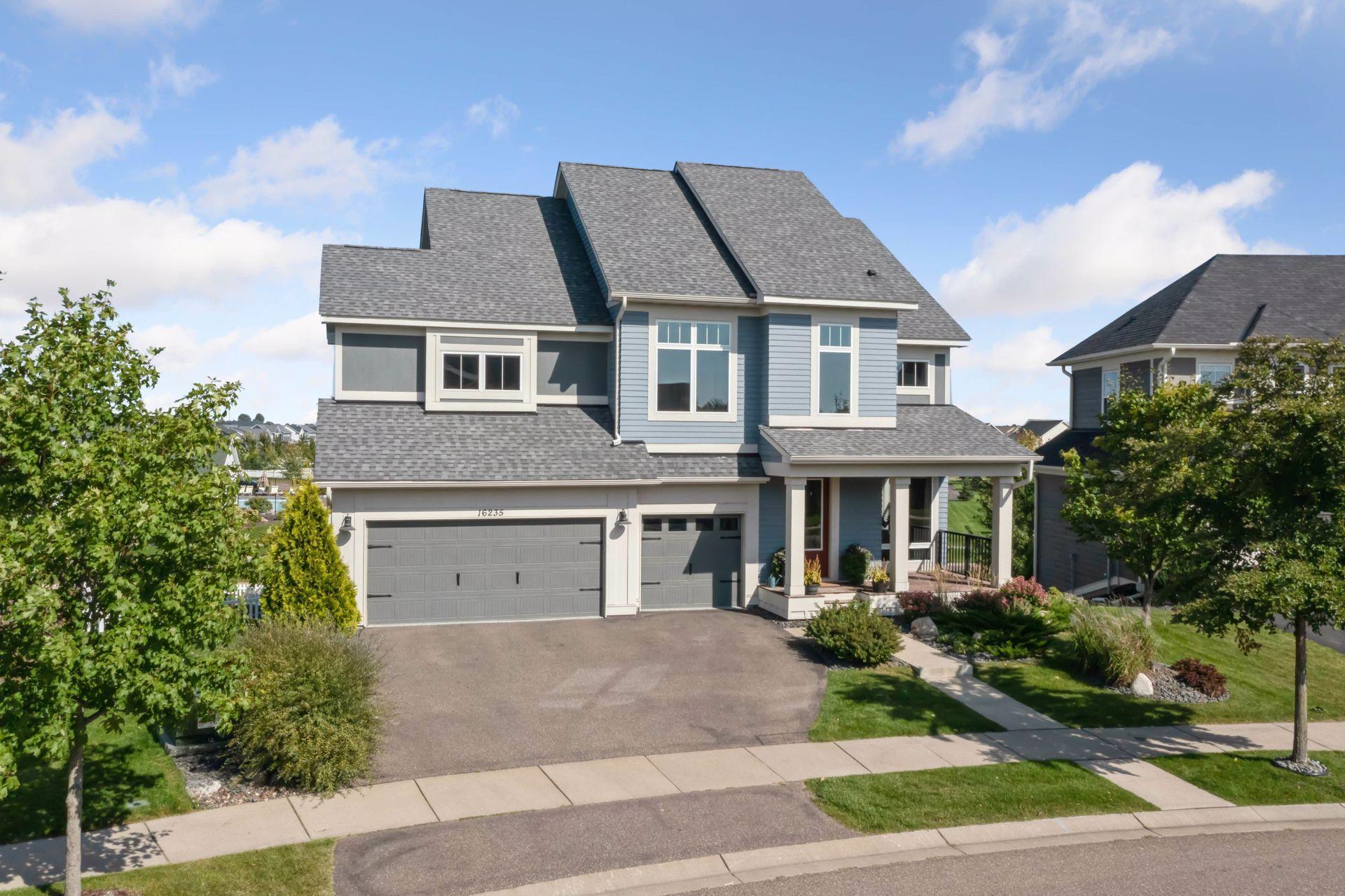 Two-story blue-gray house with a complex roof, three-car garage, and covered front porch.
