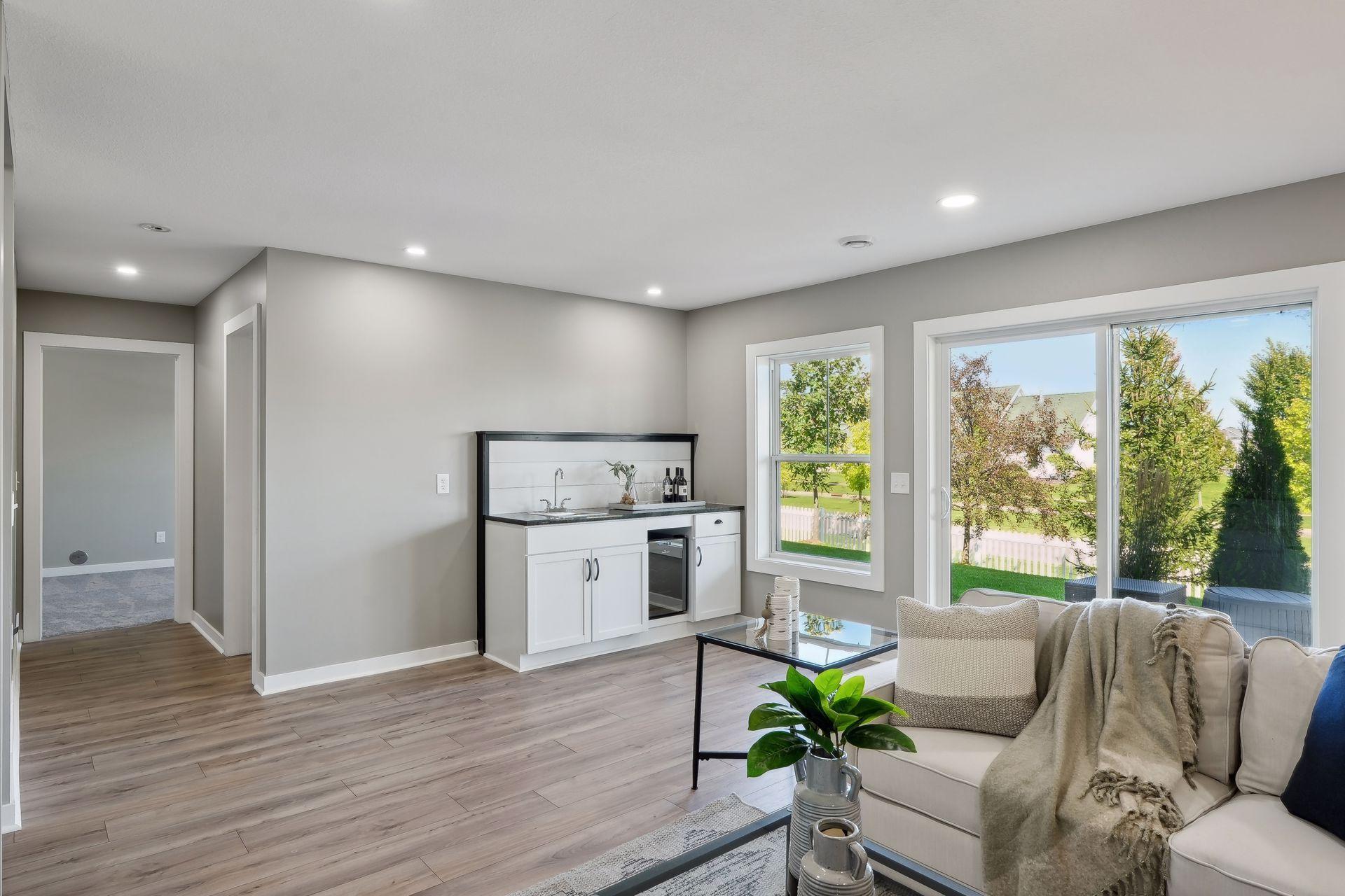 Staged living room with a built-in beverage bar, large windows, and a sofa seating area.