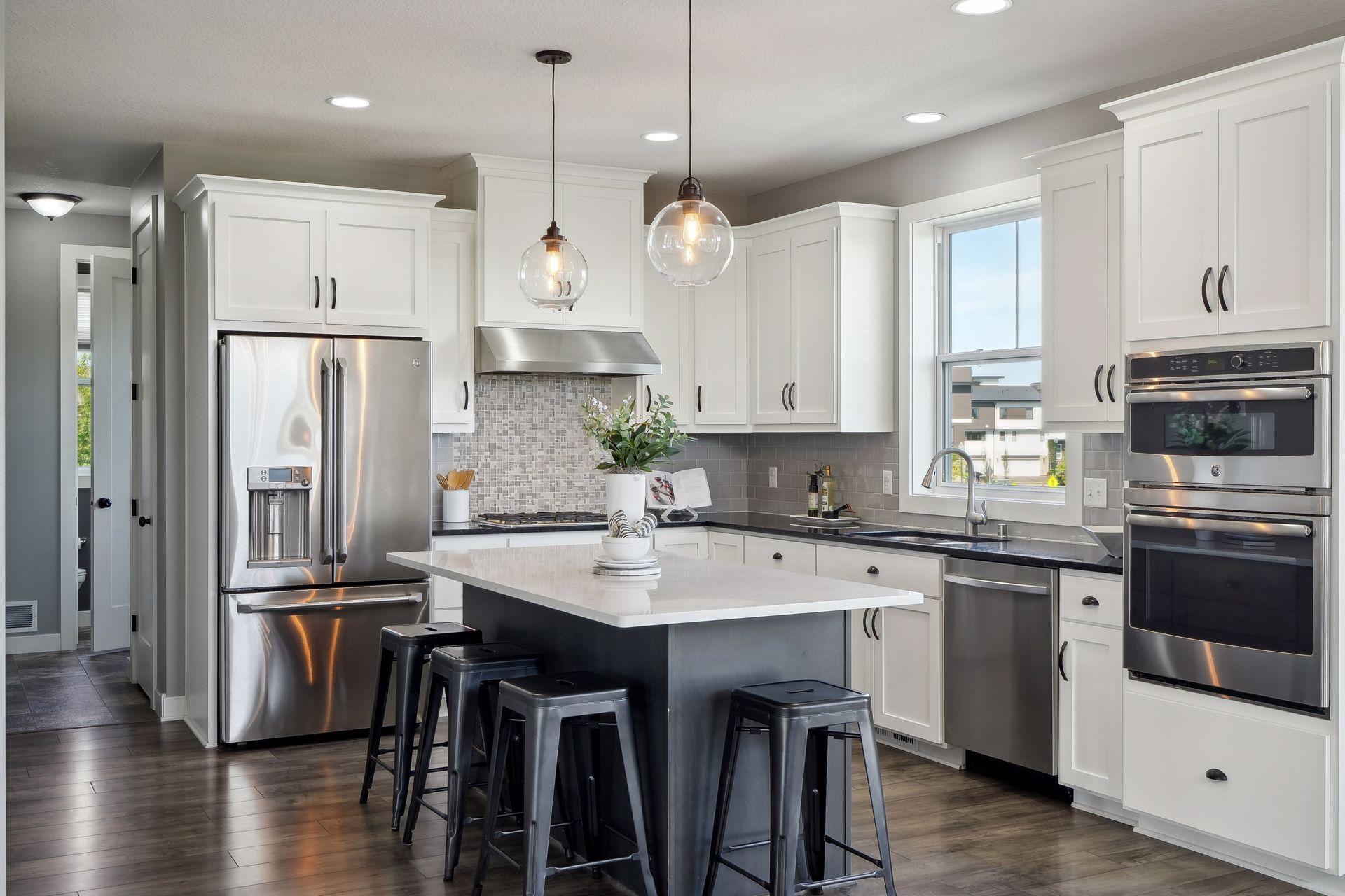 Modern kitchen with a large island, white cabinets, stainless steel appliances, and glass pendant lights.