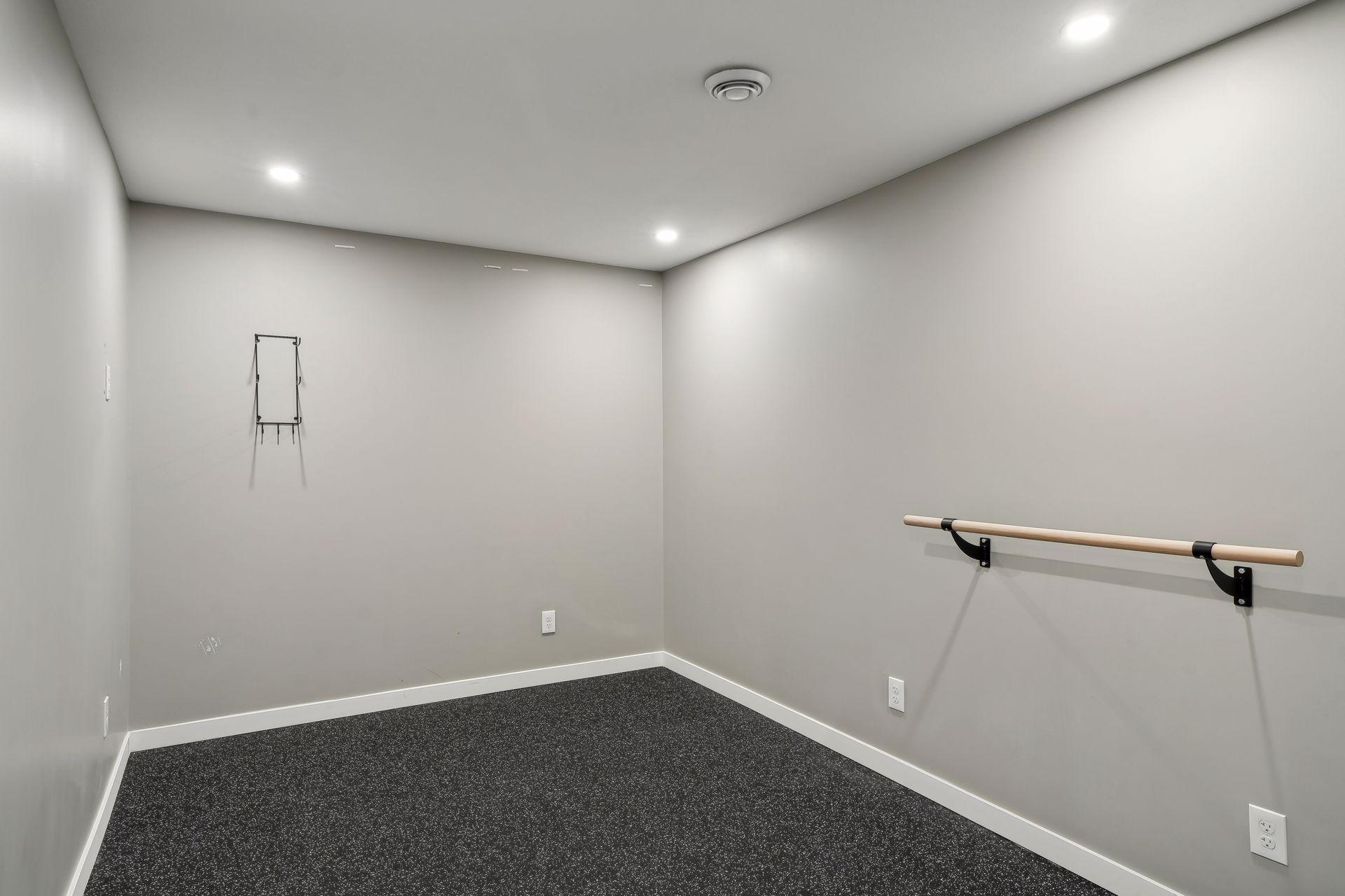 Empty exercise room with a wall-mounted wooden ballet barre and dark speckled flooring.