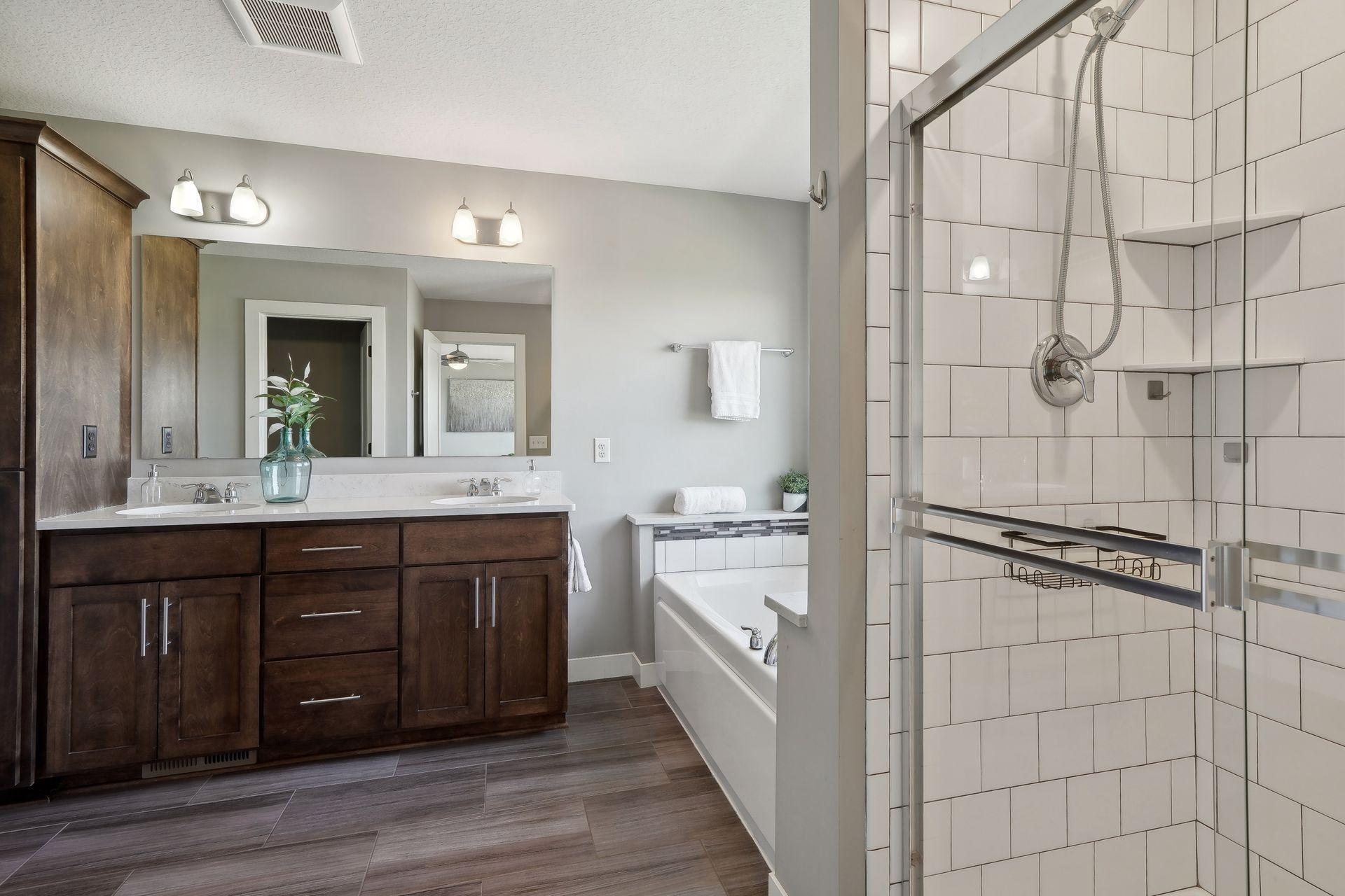 Bathroom with a dark double vanity, soaking tub, and white-tiled glass shower.