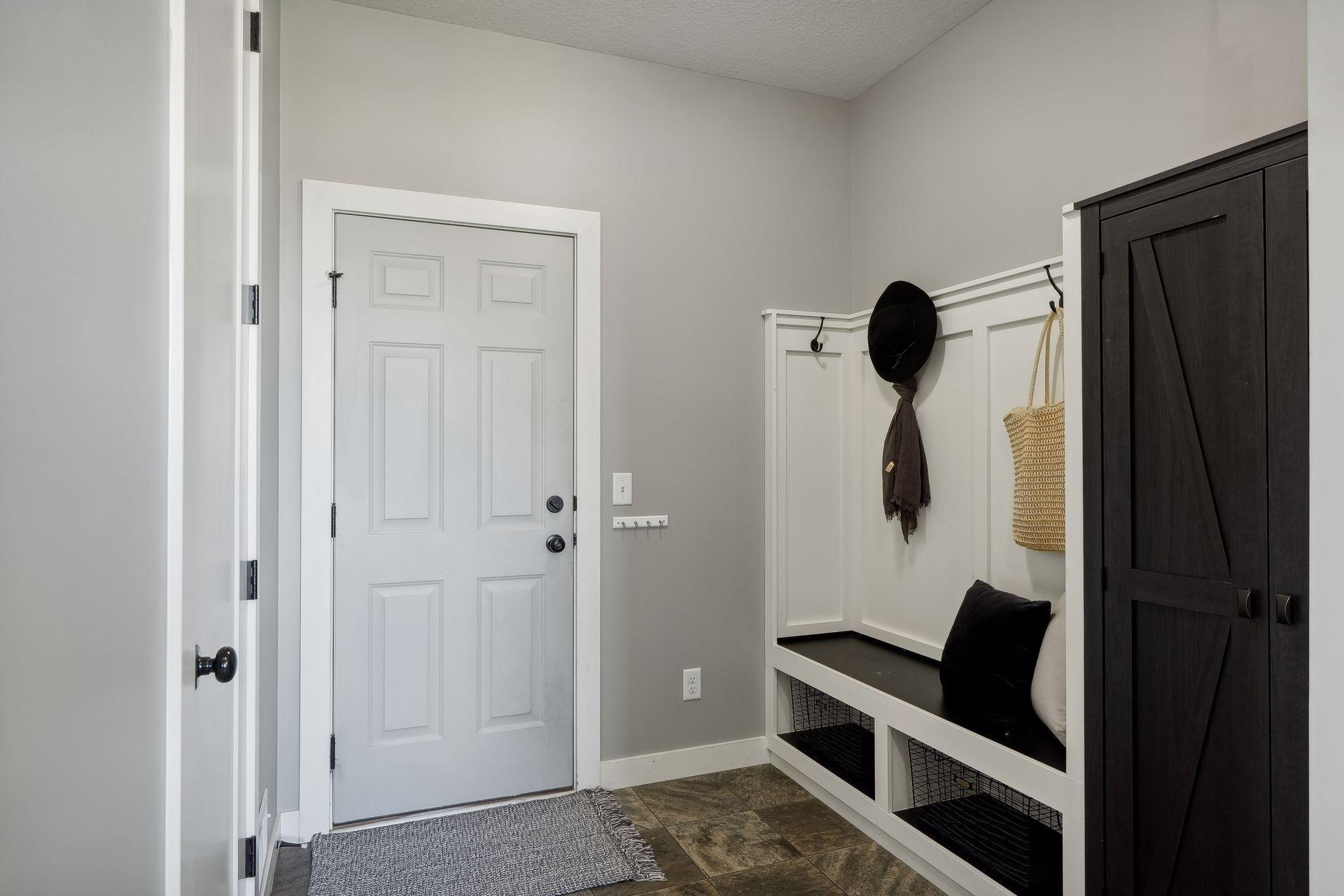 Entryway with a white front door, built-in bench and hooks, dark storage cabinet, and tiled floor.