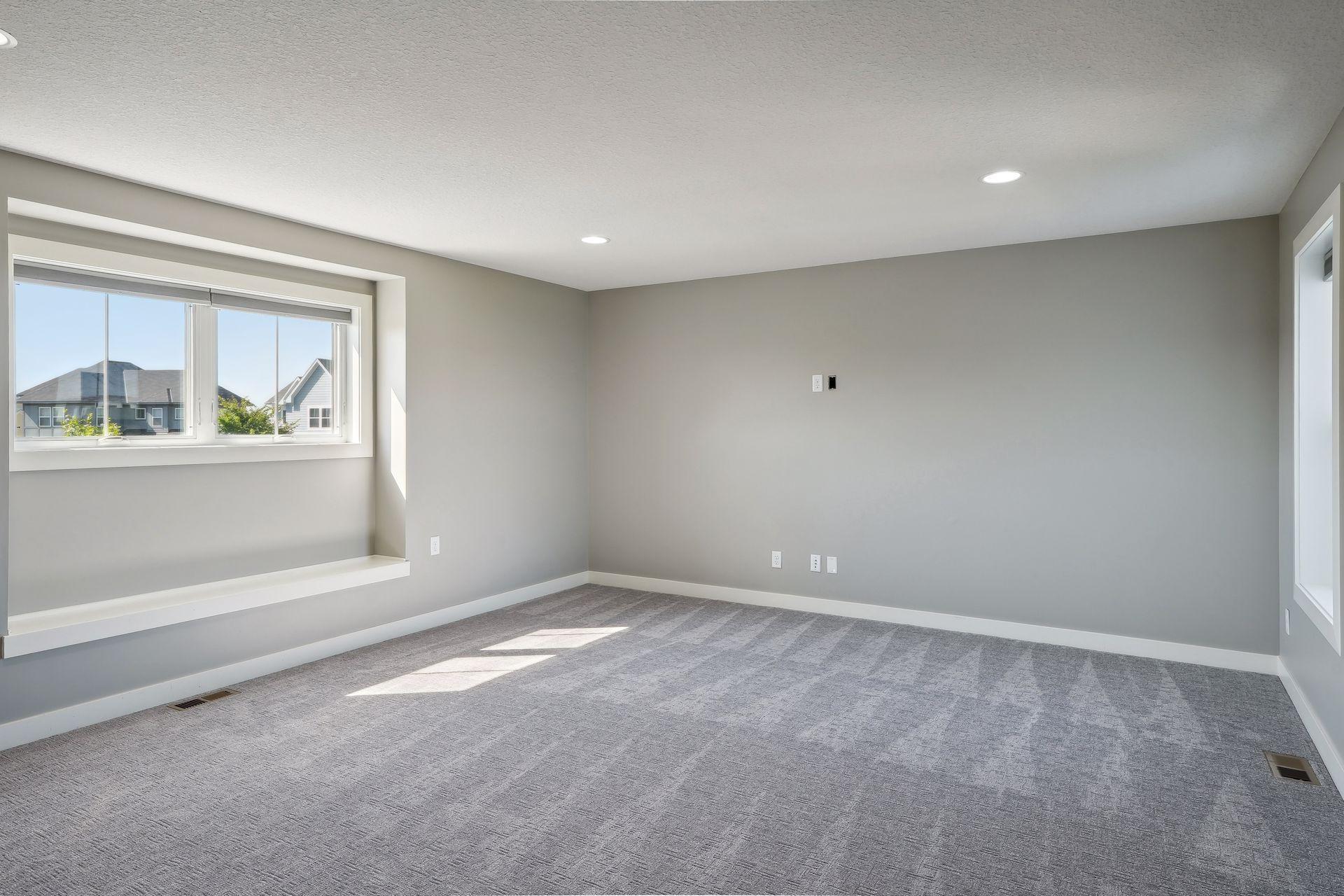 Empty carpeted room with gray walls, recessed lights, and a large window alcove.