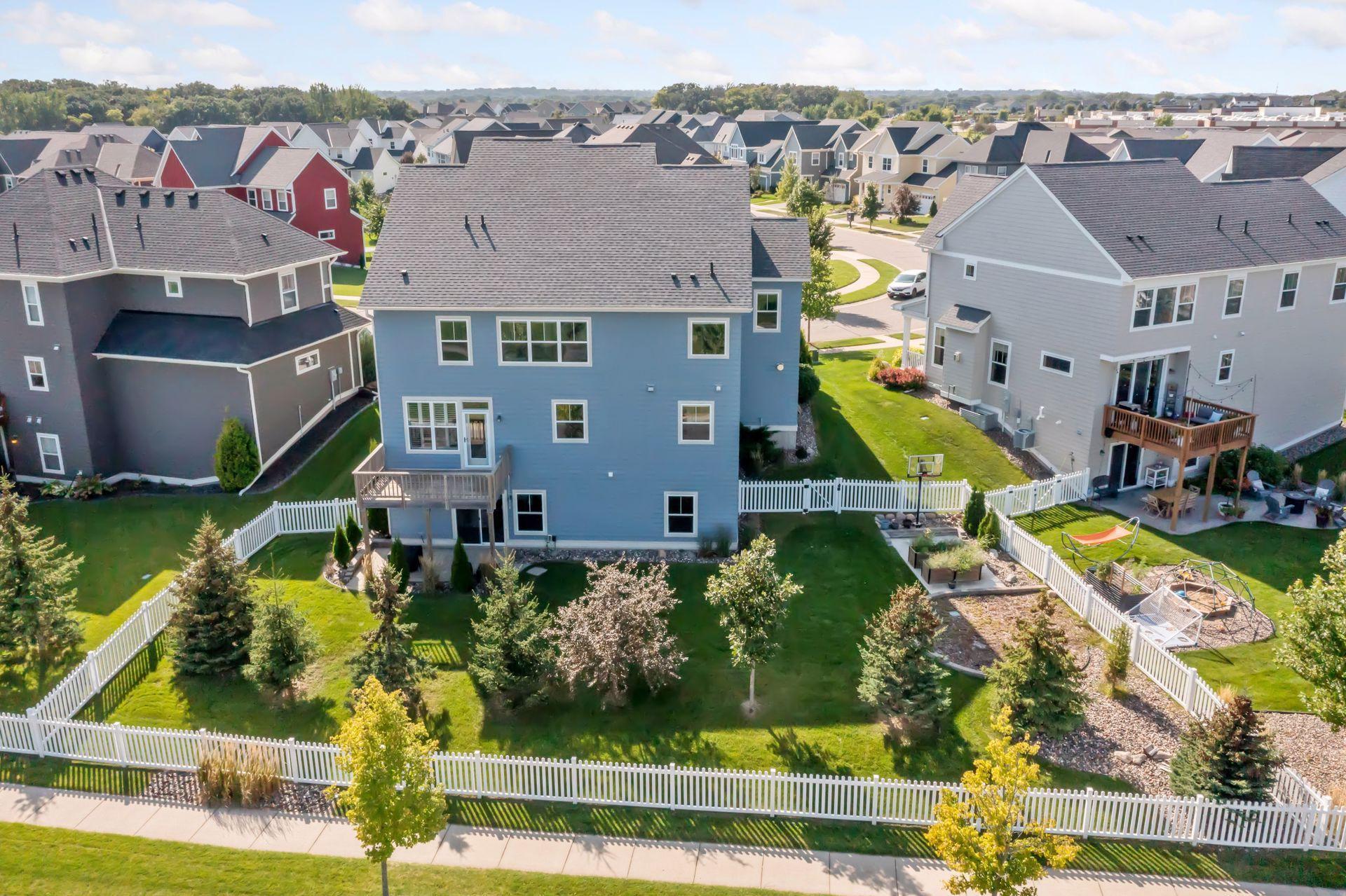 Aerial view of a blue home with a fenced backyard, deck, and landscaped lawn.