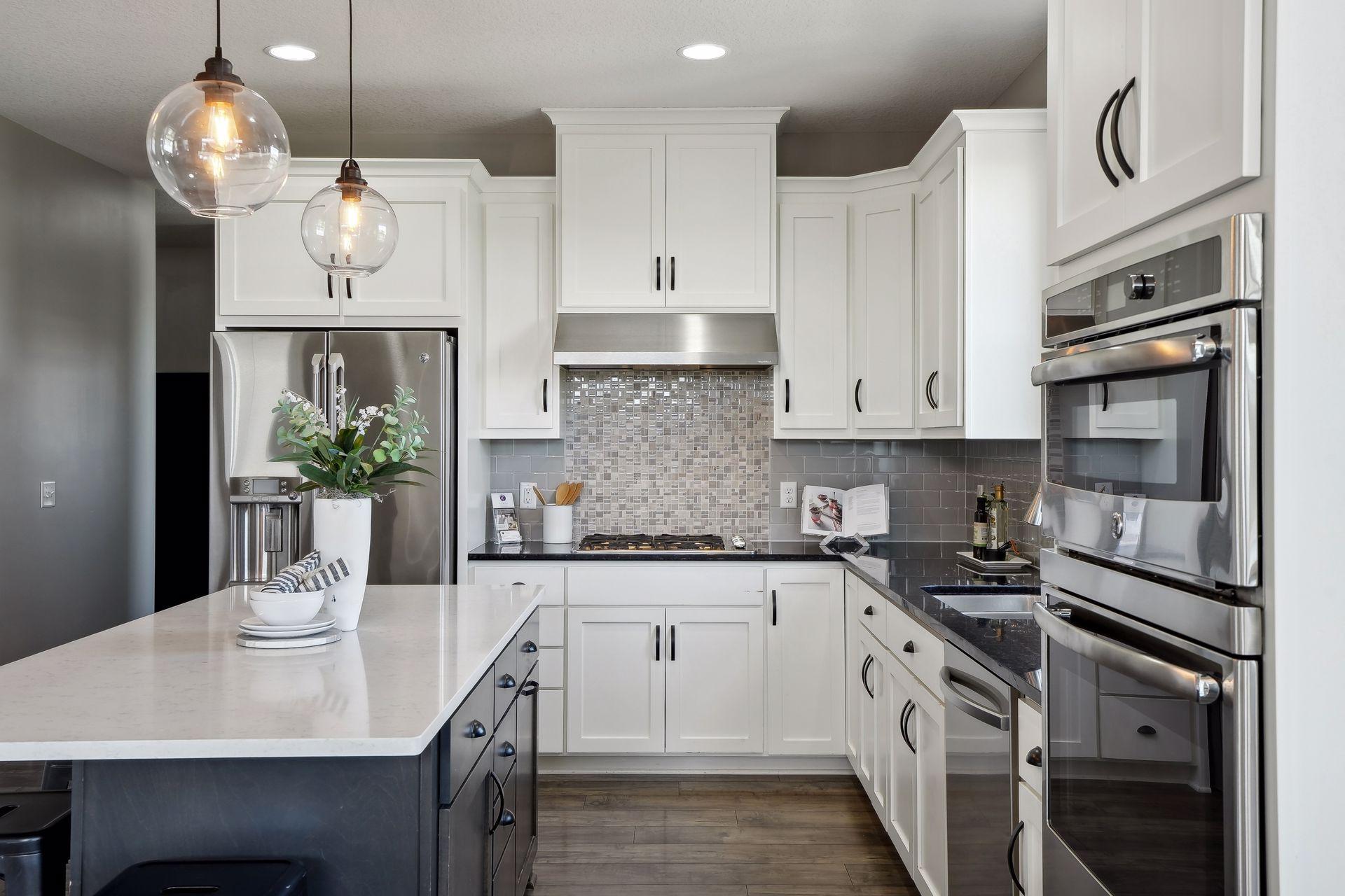 Modern white kitchen with a large island, stainless steel appliances, and a gray mosaic backsplash.
