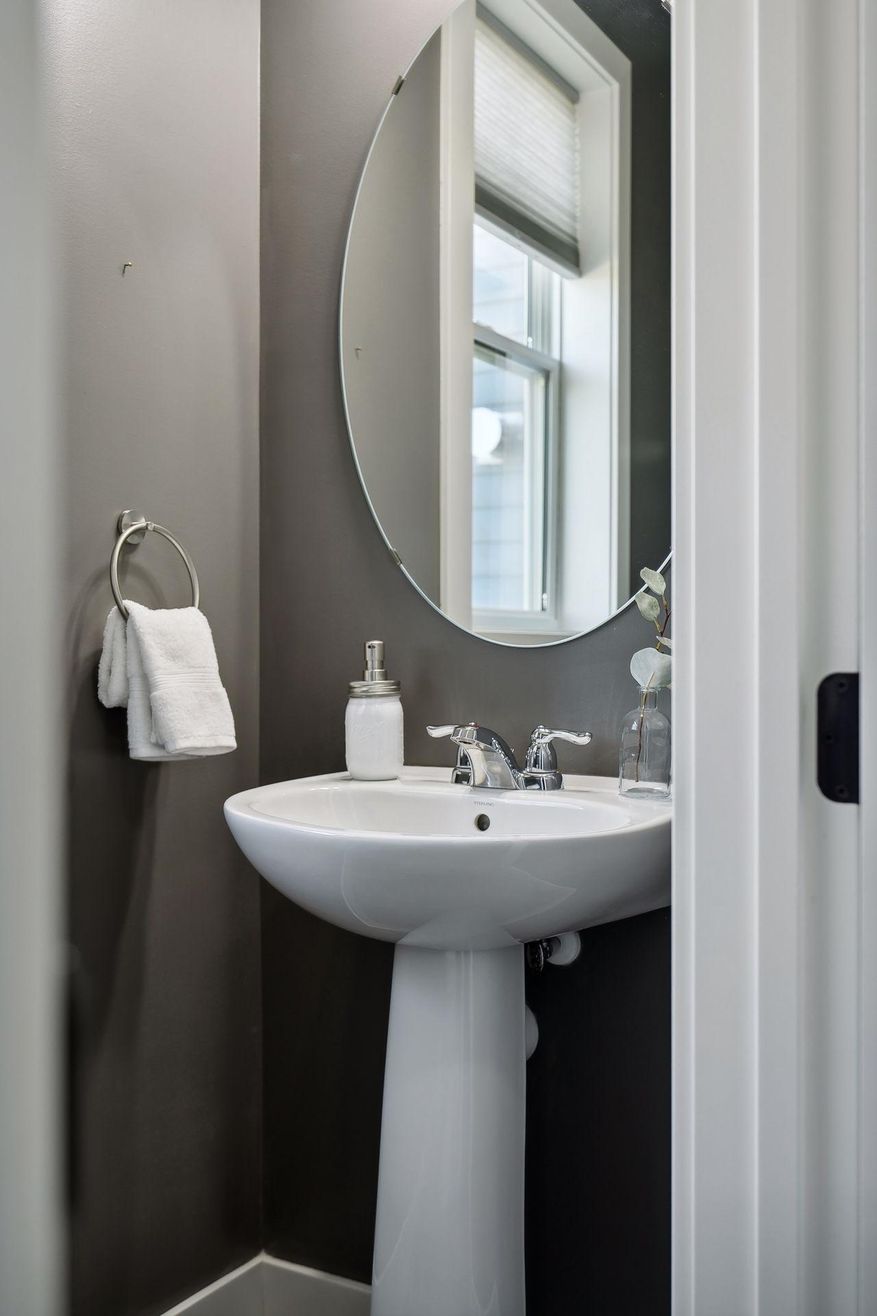 Bathroom pedestal sink beneath an oval mirror, with a white towel on a chrome ring.