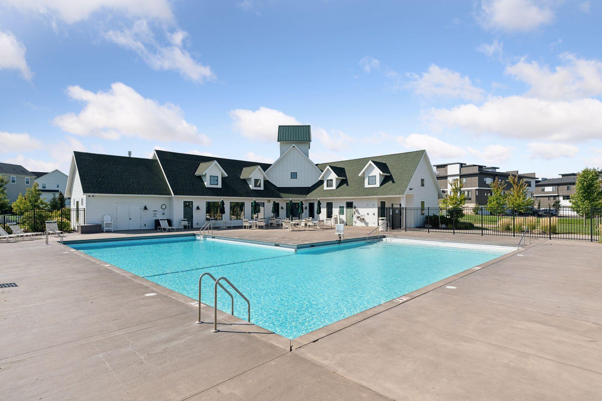 Outdoor swimming pool with a white poolhouse, lounge chairs, and fenced deck.