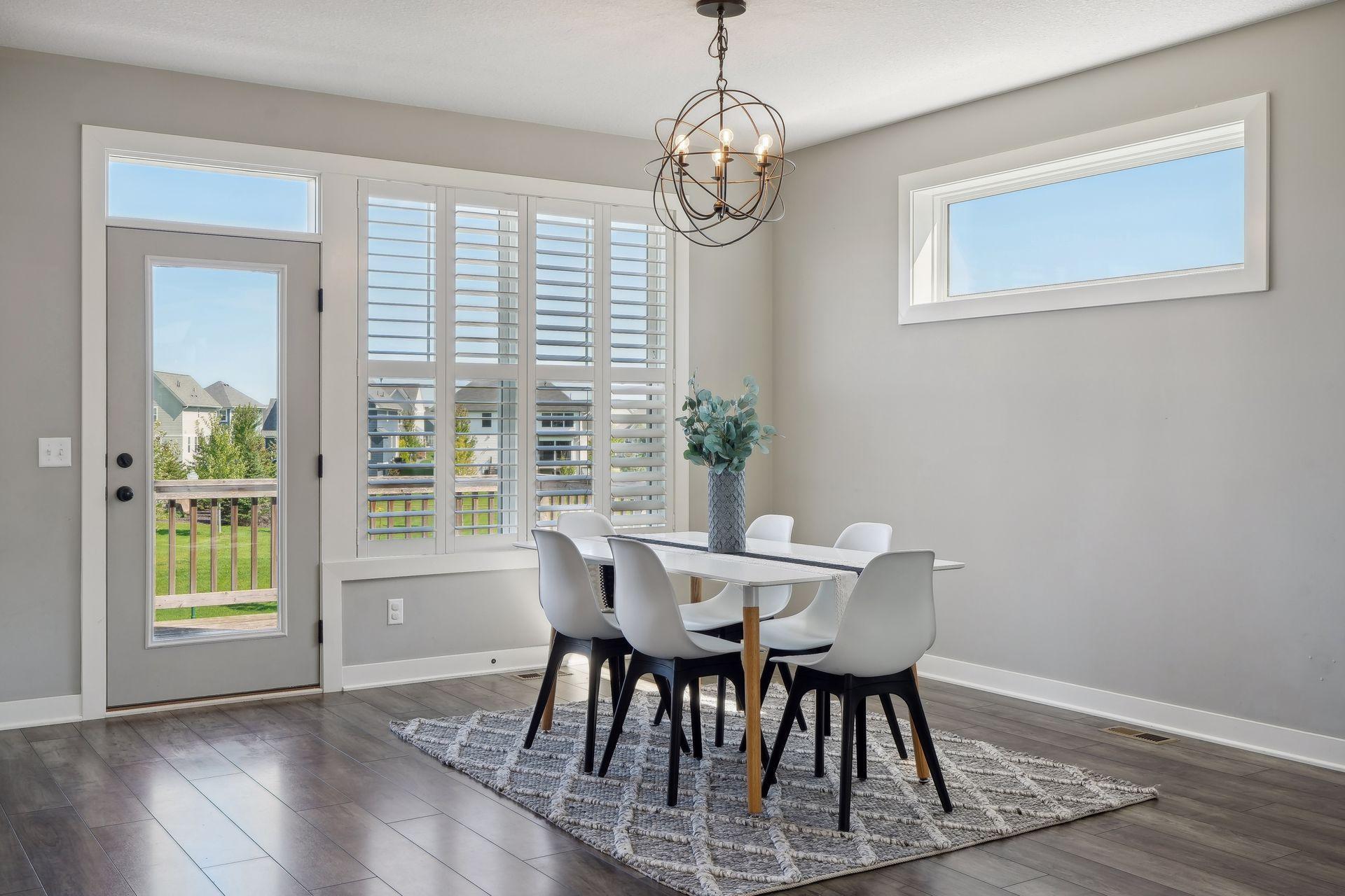 Dining room with white chairs, plantation shutters, and a glass-paneled door to the deck.