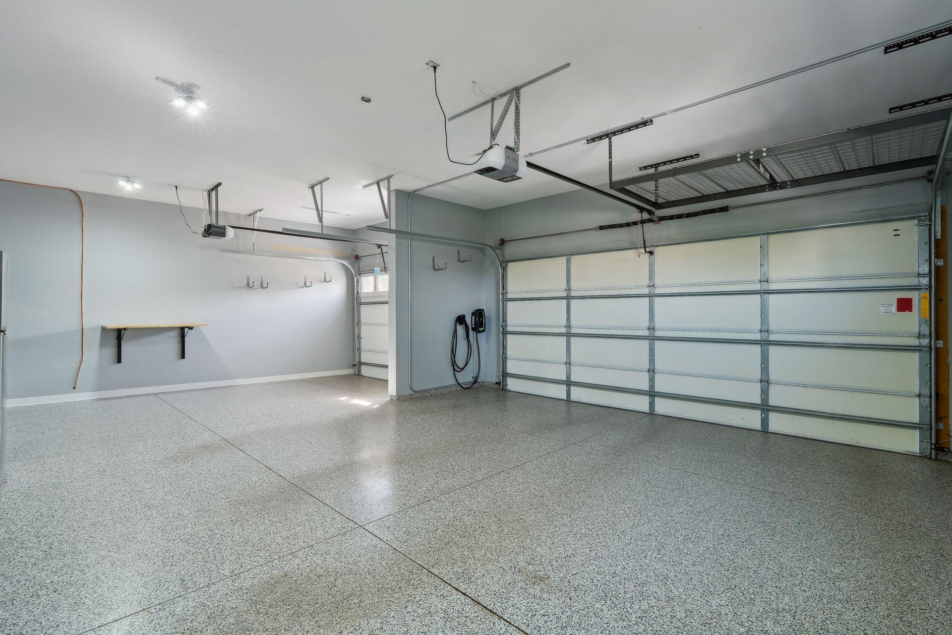 Empty two-car garage with a speckled epoxy floor, overhead storage racks, and an electric vehicle charger.