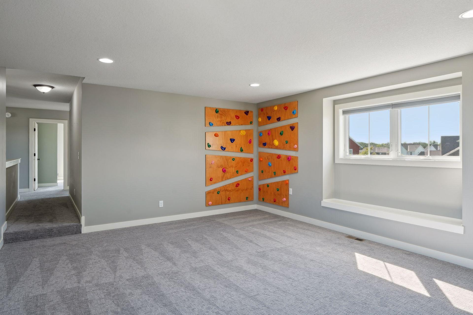 Vacant recreation room with a colorful climbing wall and large window.