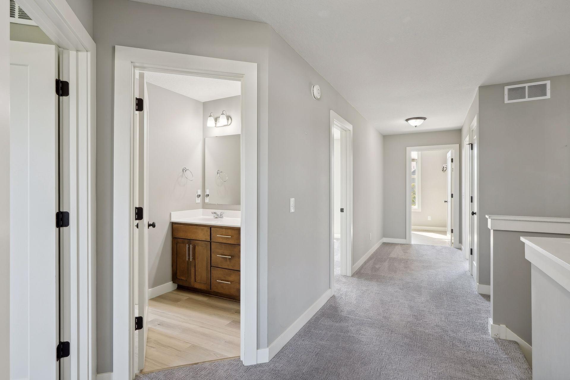 Carpeted hallway with an open bathroom doorway showing a dark wood vanity.