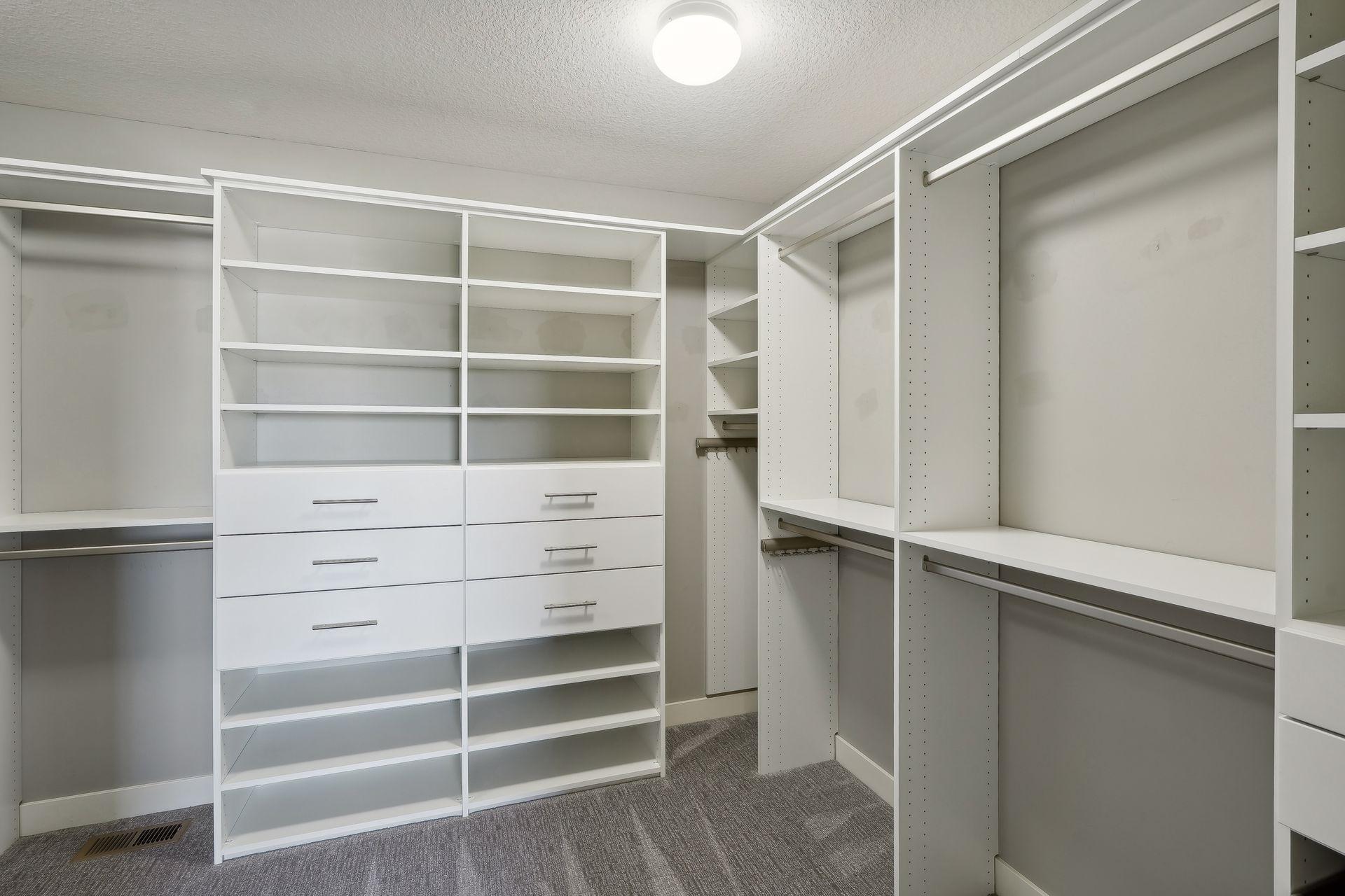 Walk-in closet with white built-in shelves, drawers, hanging rods, and gray carpet.