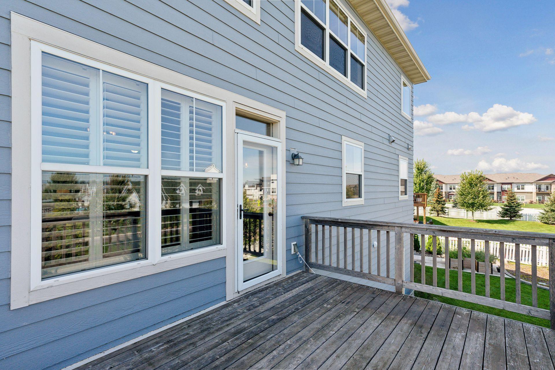 Blue-gray home exterior with a wooden deck, shuttered windows, and glass patio door.