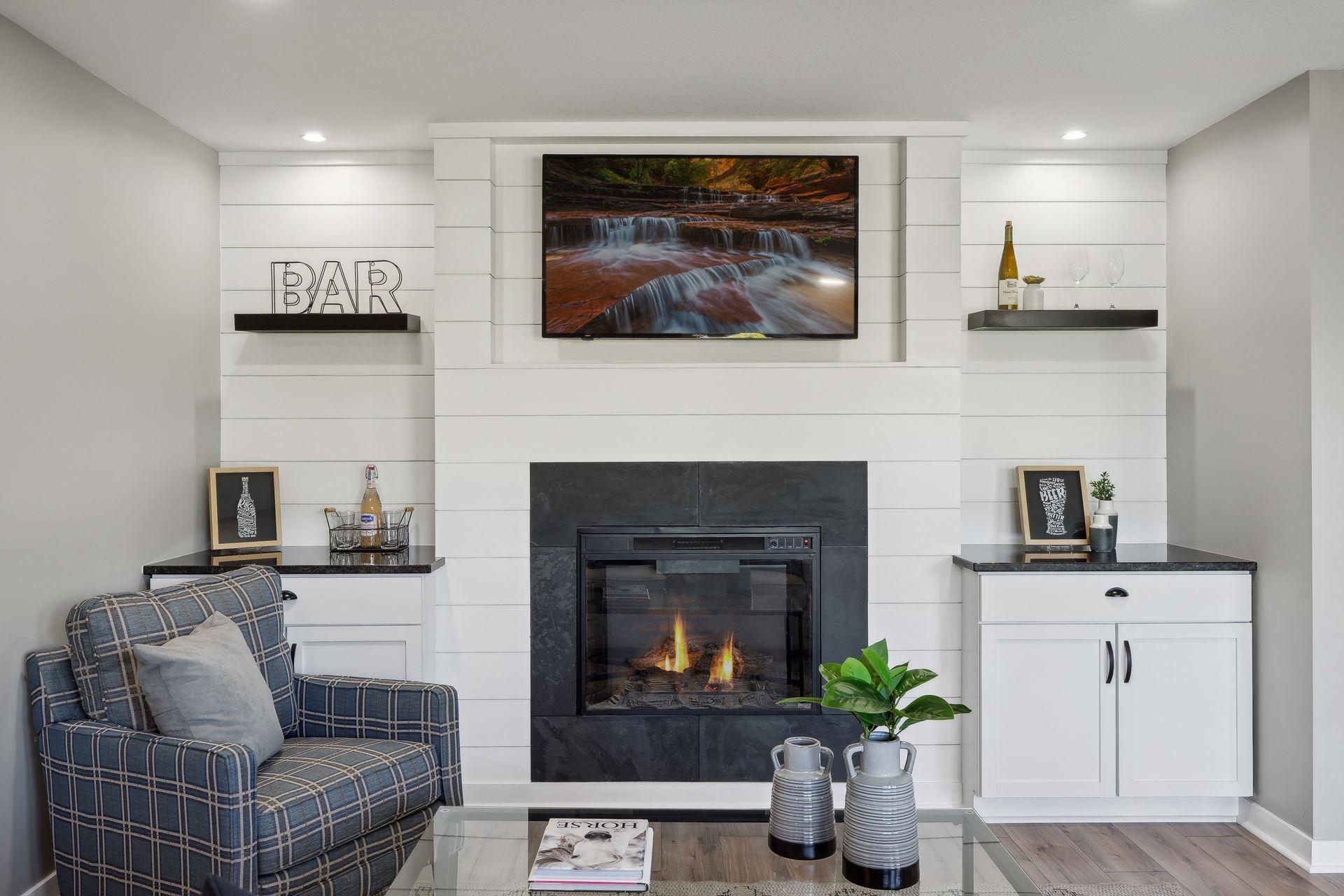 Living room with a stone fireplace, television, white built-ins, and plaid armchair.