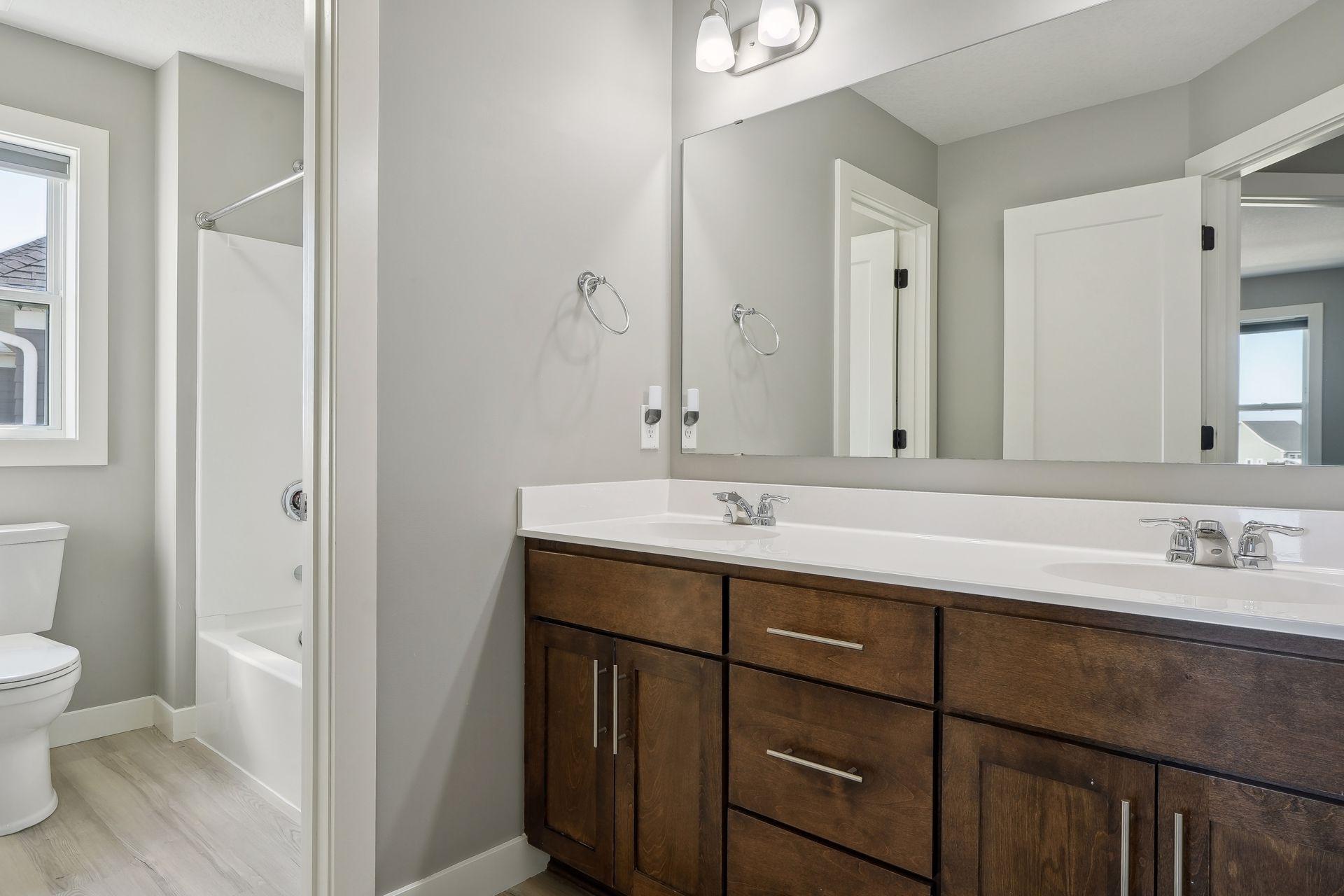 Bathroom with a dark wood double vanity, large mirror, and tub-shower beside a window.