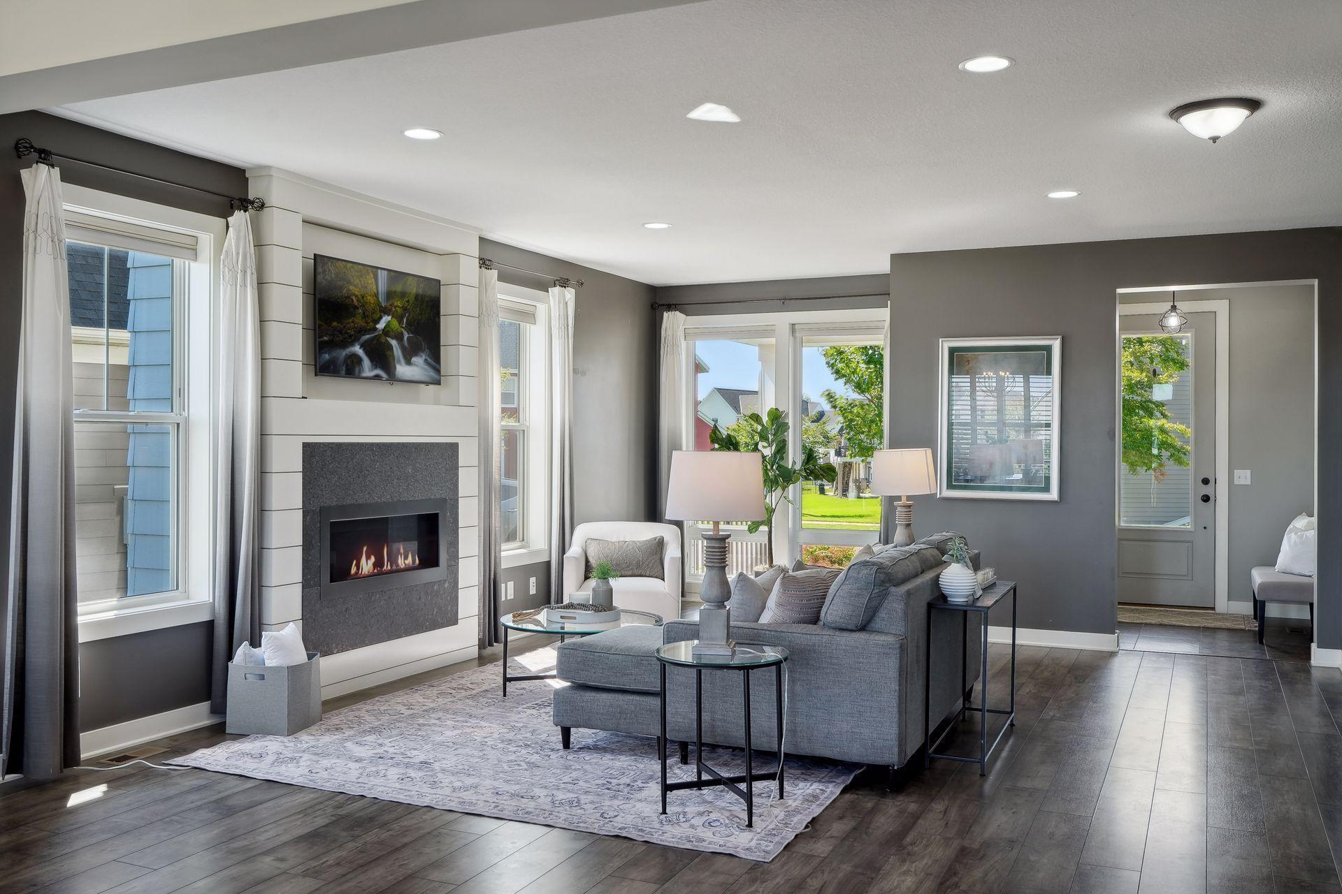 Living room with a gray sectional, modern fireplace, and large windows overlooking a lawn.